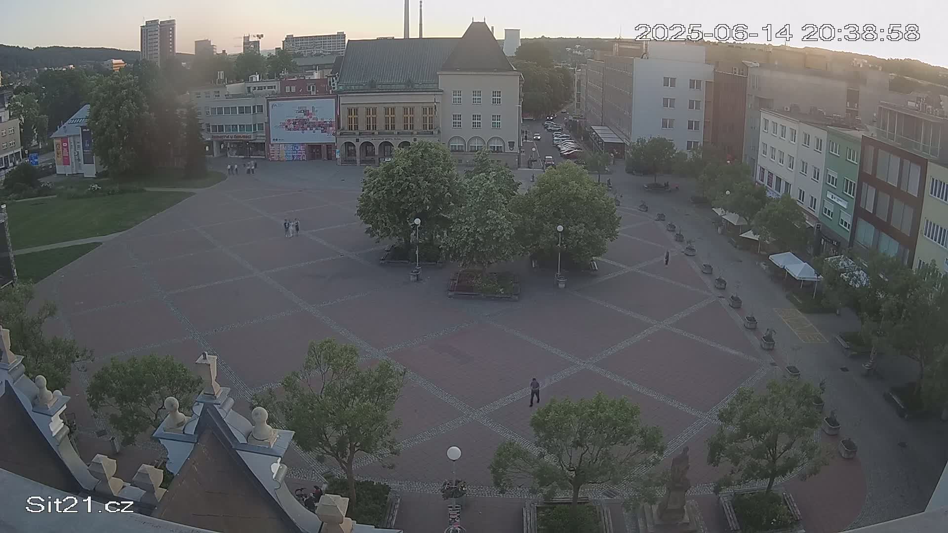 A large, brick-paved town square with several buildings and trees surrounding it on a sunny day.