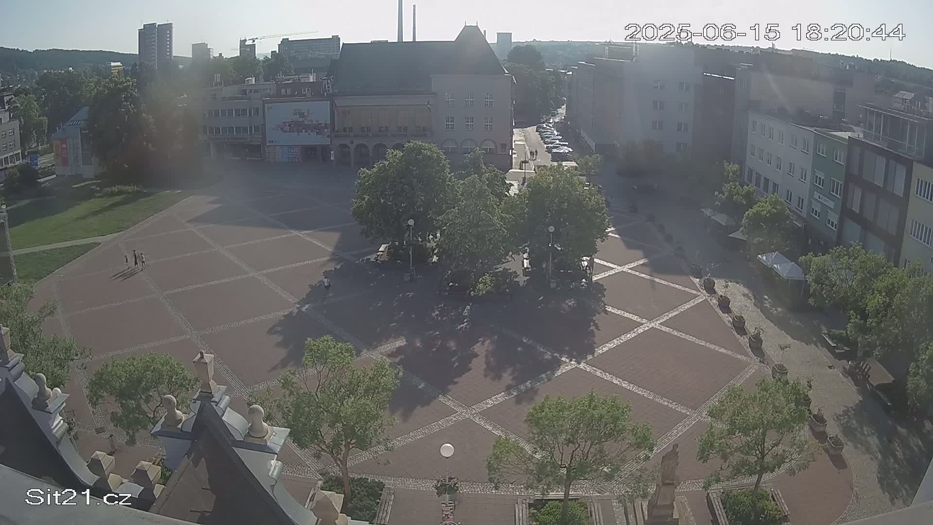 A paved town square with several trees and buildings surrounding it on a sunny day.