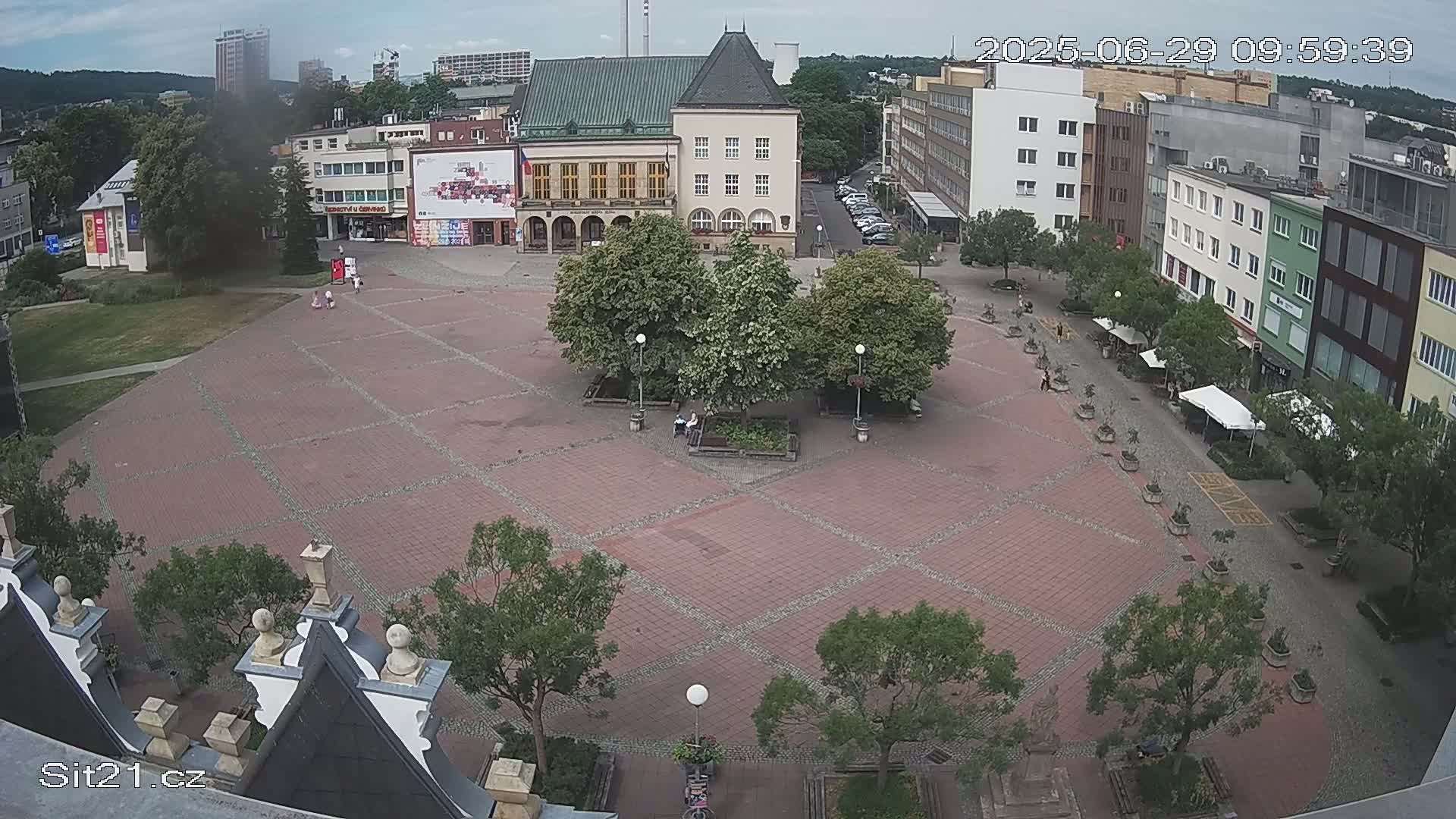 A brick town square with several trees and buildings surrounding it on a partly cloudy day.