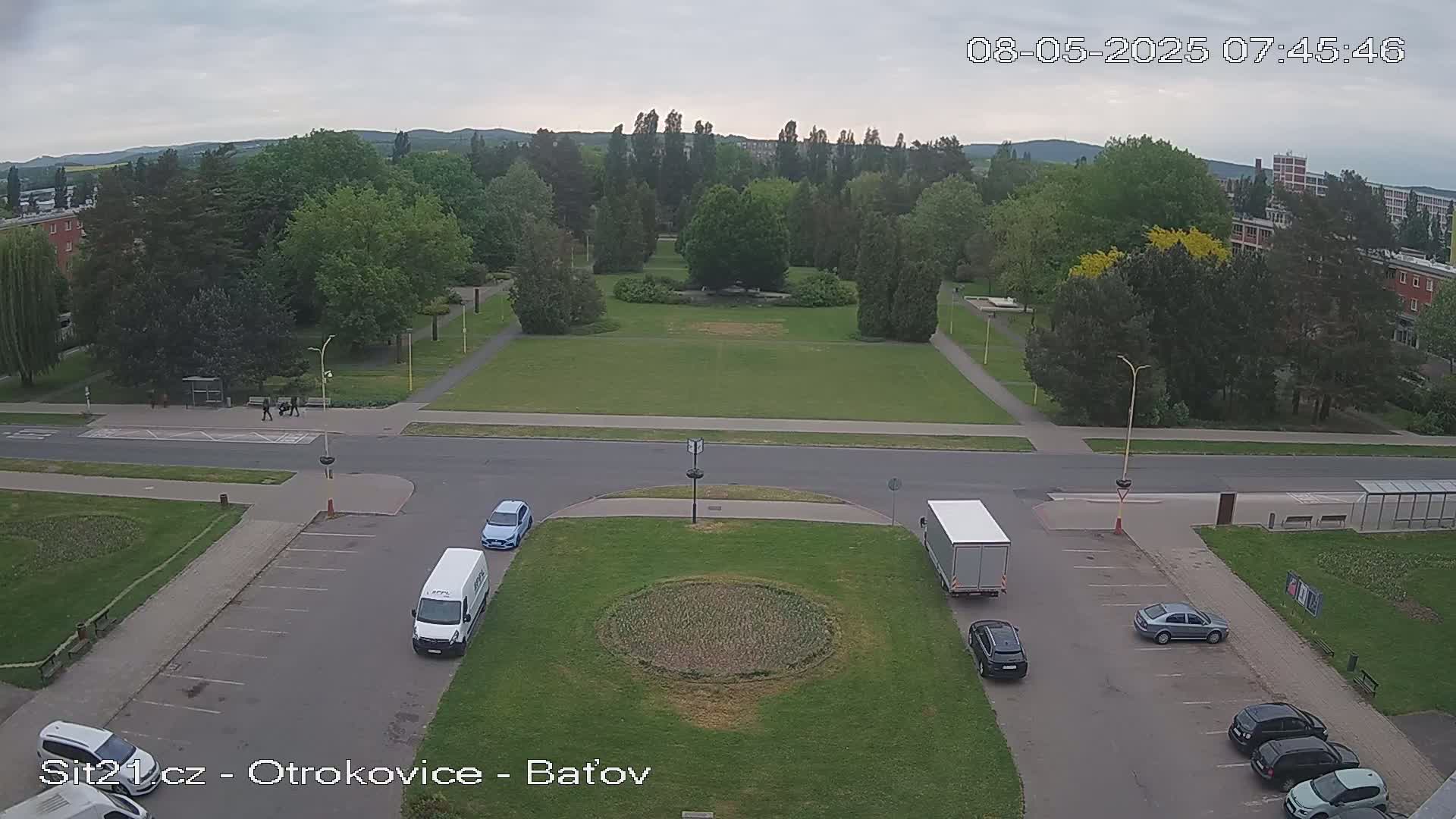 An overcast day reveals a high-angle view of a park, a street, and parking lots with several vehicles, including a van and a truck.