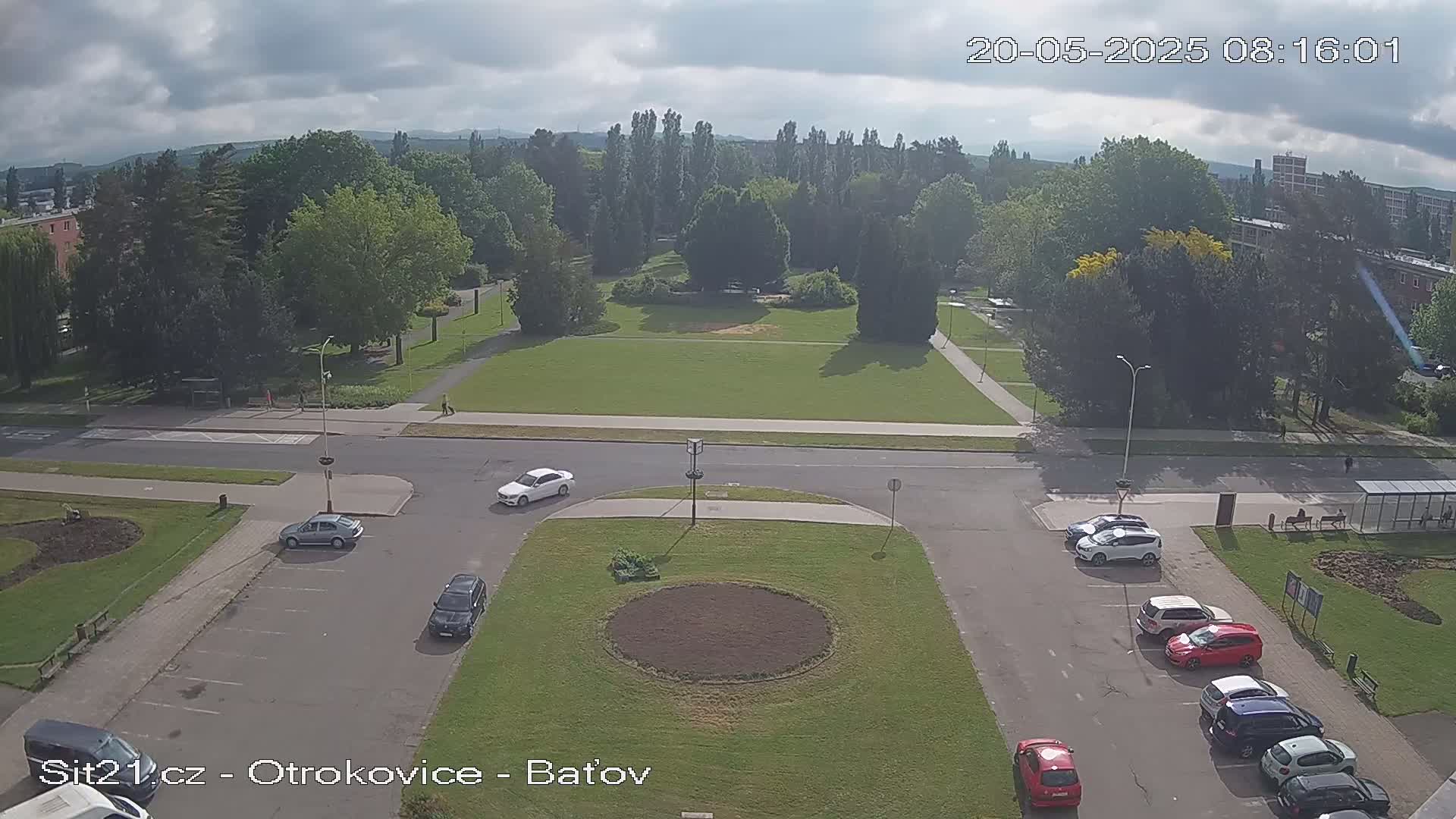 An aerial view of a park and parking lot with several cars, under a partly cloudy sky.