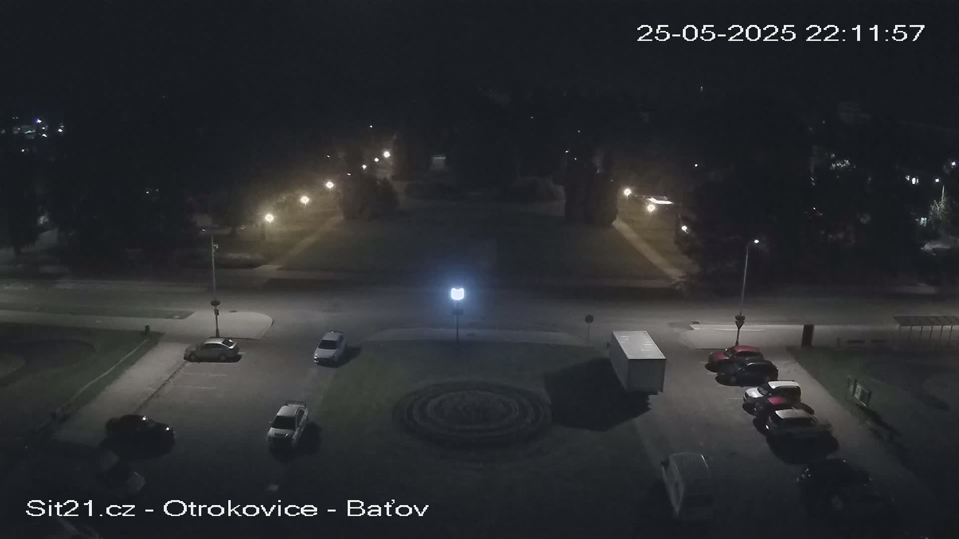 A nighttime aerial view of a parking lot with several cars and a truck, surrounded by trees and streetlights.