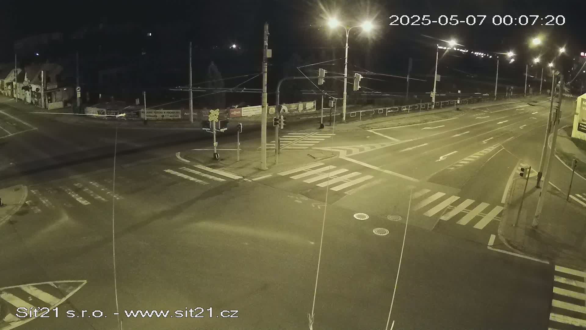 A nighttime view of a deserted street intersection with crosswalks and traffic lights under artificial street lighting.