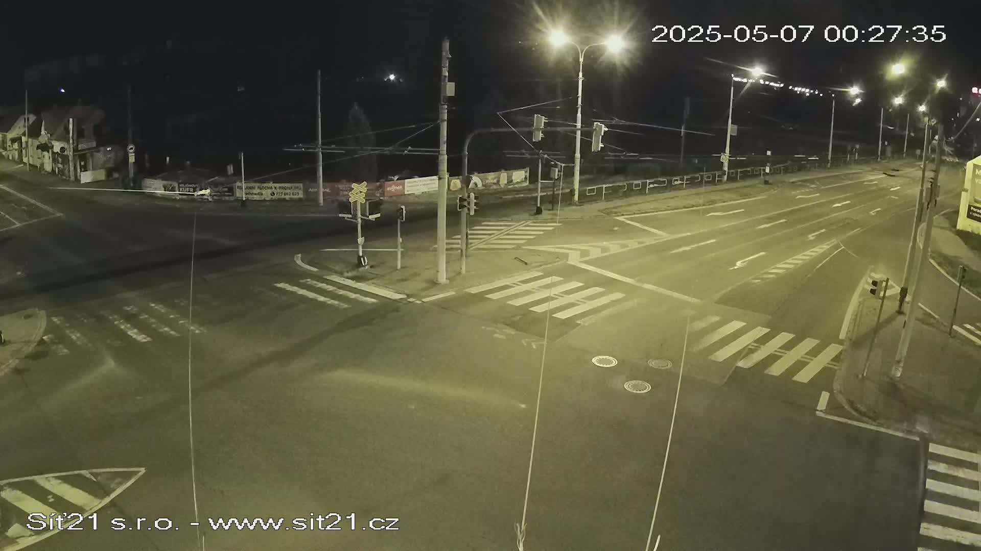 A nighttime view of a multi-lane road intersection with crosswalks, traffic lights, and streetlights.
