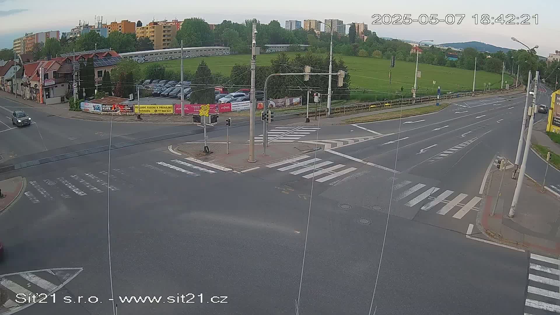 A mostly empty multi-lane road intersection with crosswalks, traffic lights, and a few cars, under an overcast sky, is viewed from above.