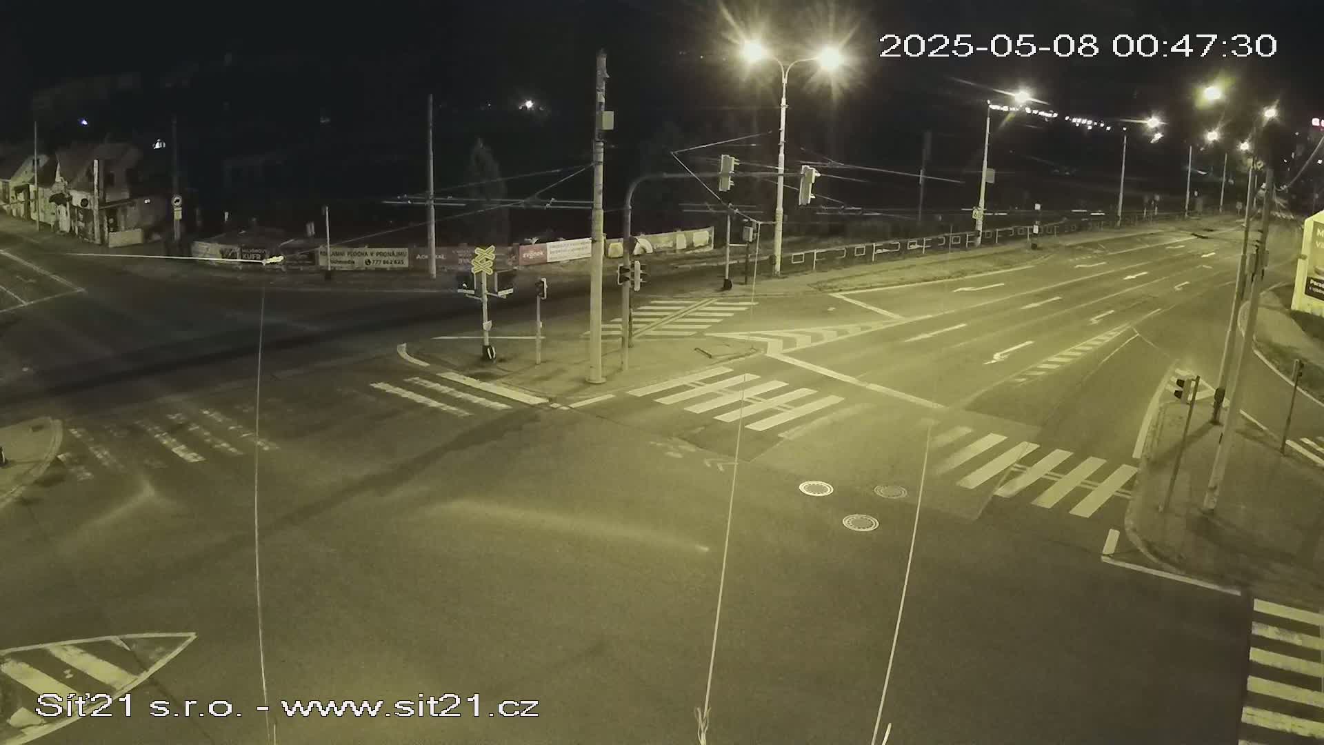 A nighttime view of a mostly empty street intersection with crosswalks and traffic lights under clear skies.