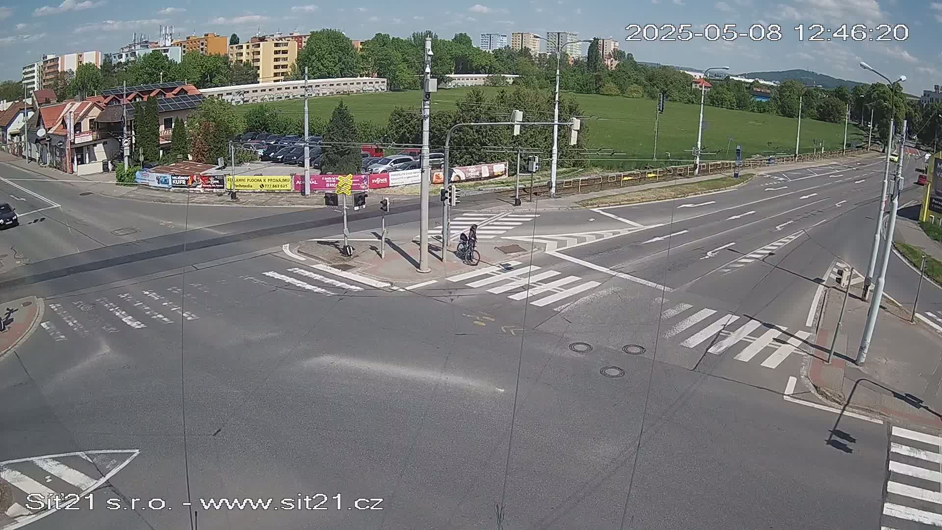 A cyclist rides through a multi-lane road intersection on a sunny day.