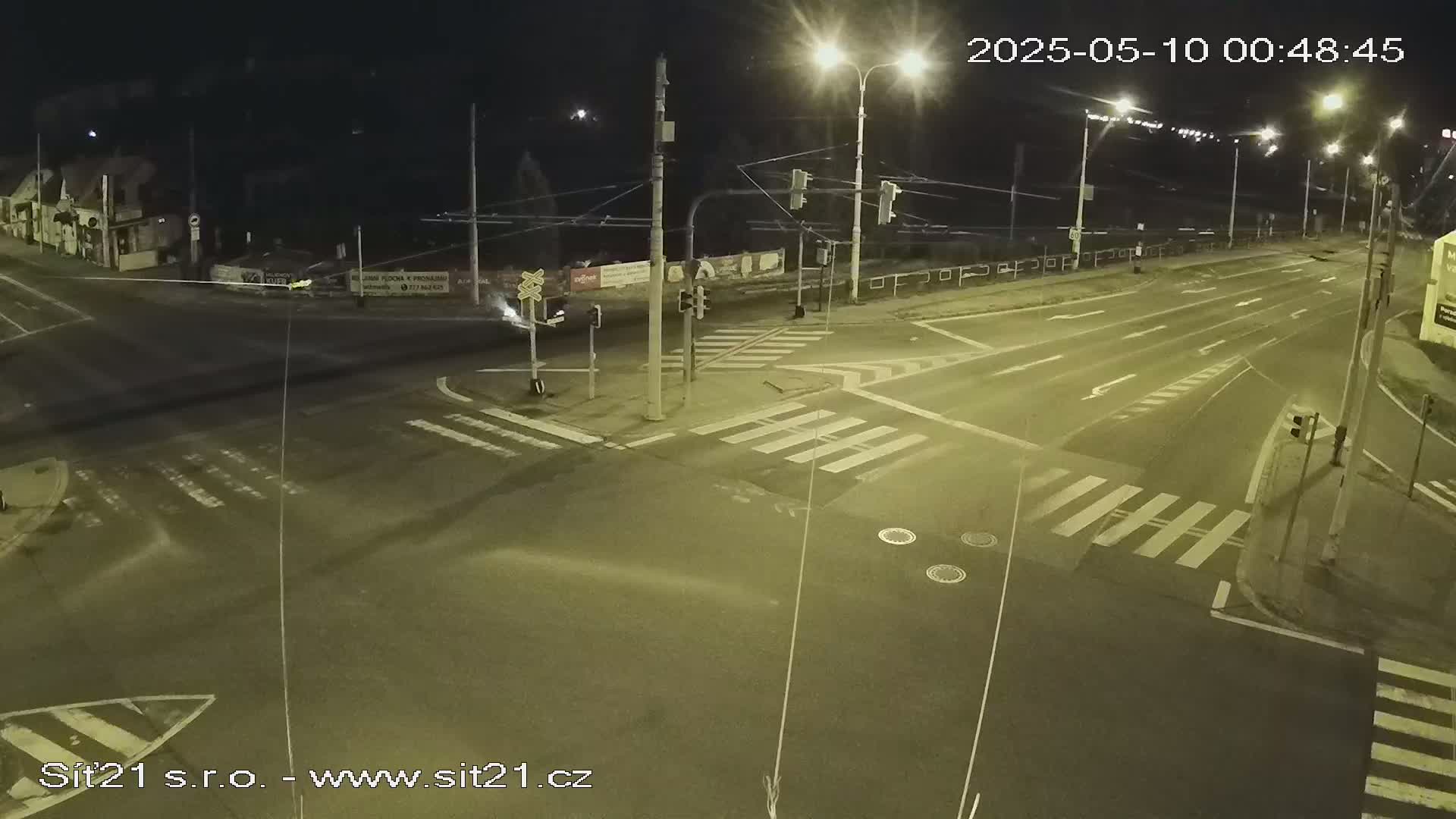 A nighttime view of a multi-lane road intersection with crosswalks and traffic signals, under clear skies.