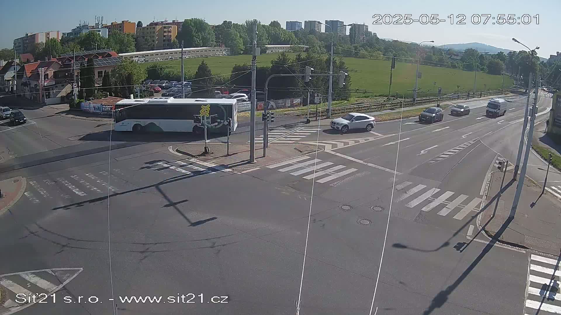 A sunny day shows a street intersection with several cars and a bus, with crosswalks and traffic signals visible.