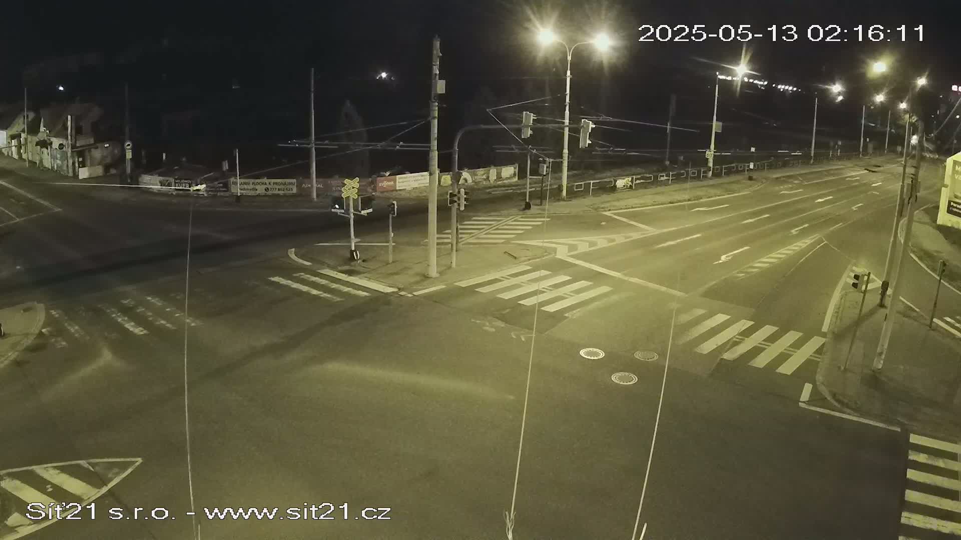 A nighttime, overhead view of a mostly empty street intersection with crosswalks and traffic lights.