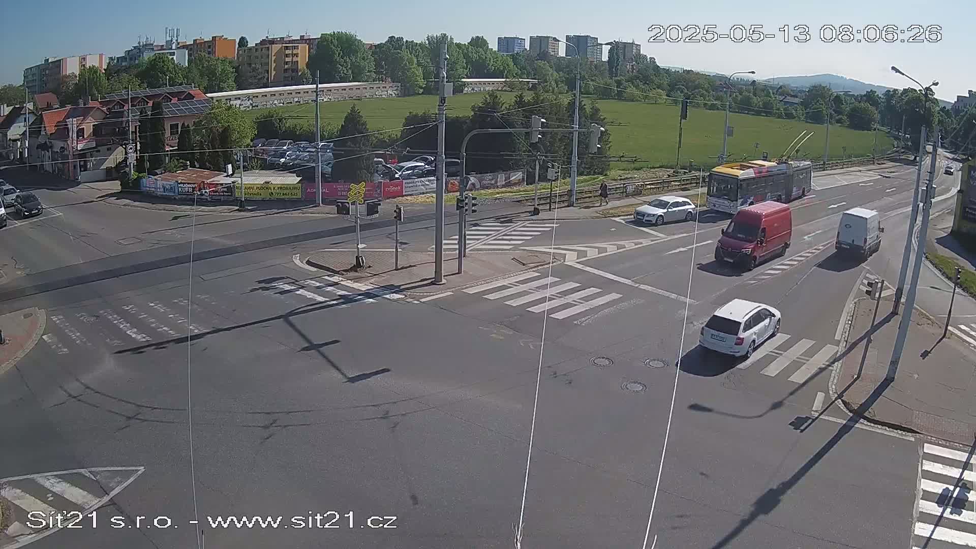 A sunny day shows a multi-lane intersection with several cars and a bus, all at a standstill at a traffic light.