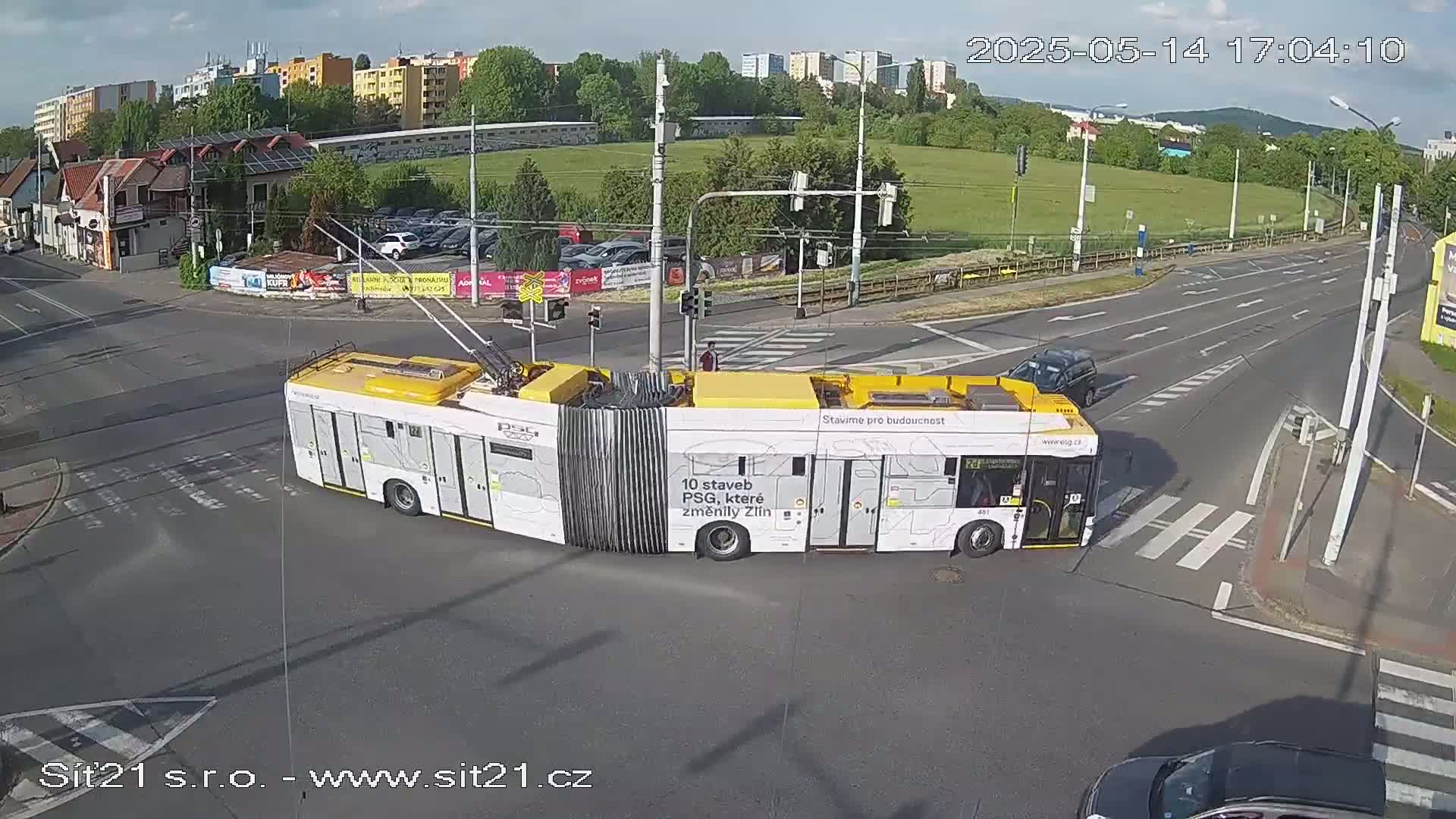 A long, yellow and white trolleybus is navigating a street intersection on a partly sunny day.