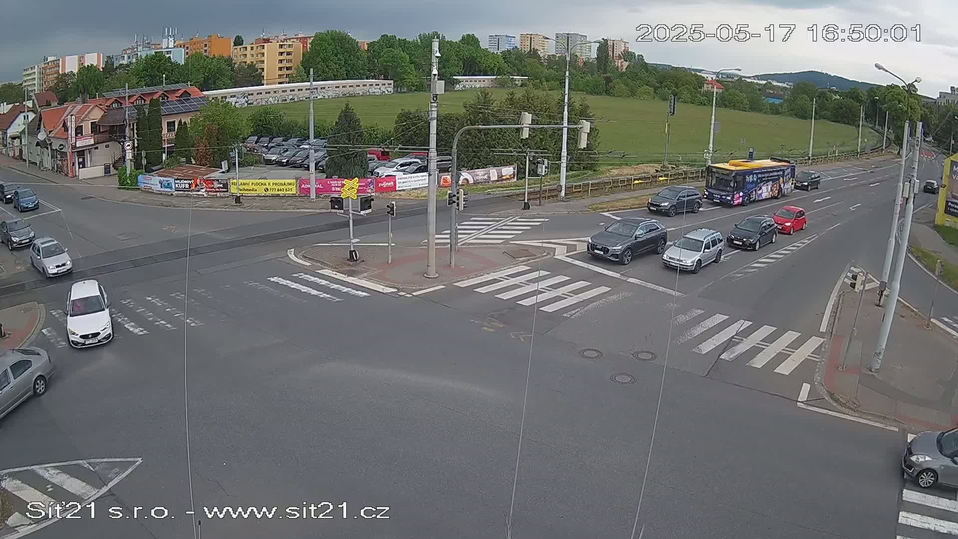 A multi-lane road intersection with several cars and a bus, under partly cloudy skies.