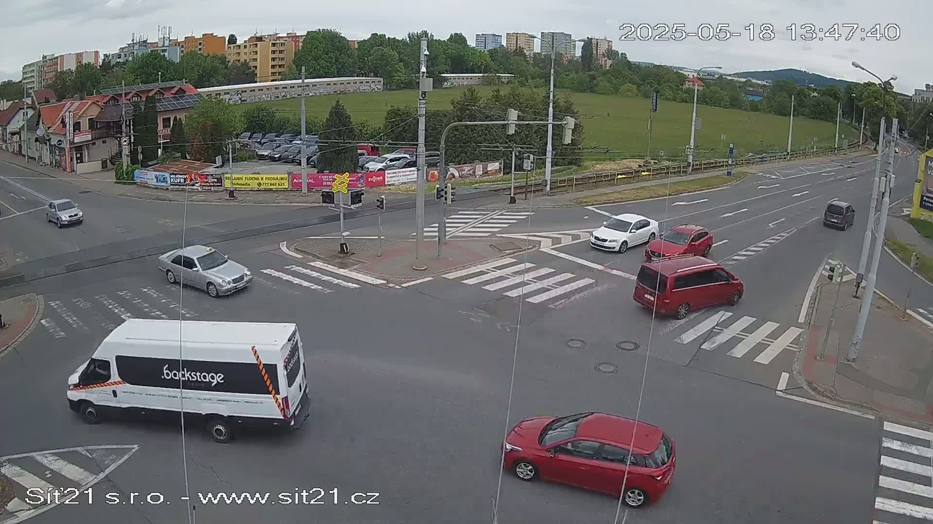 A busy road intersection with several cars and a van, under an overcast sky.