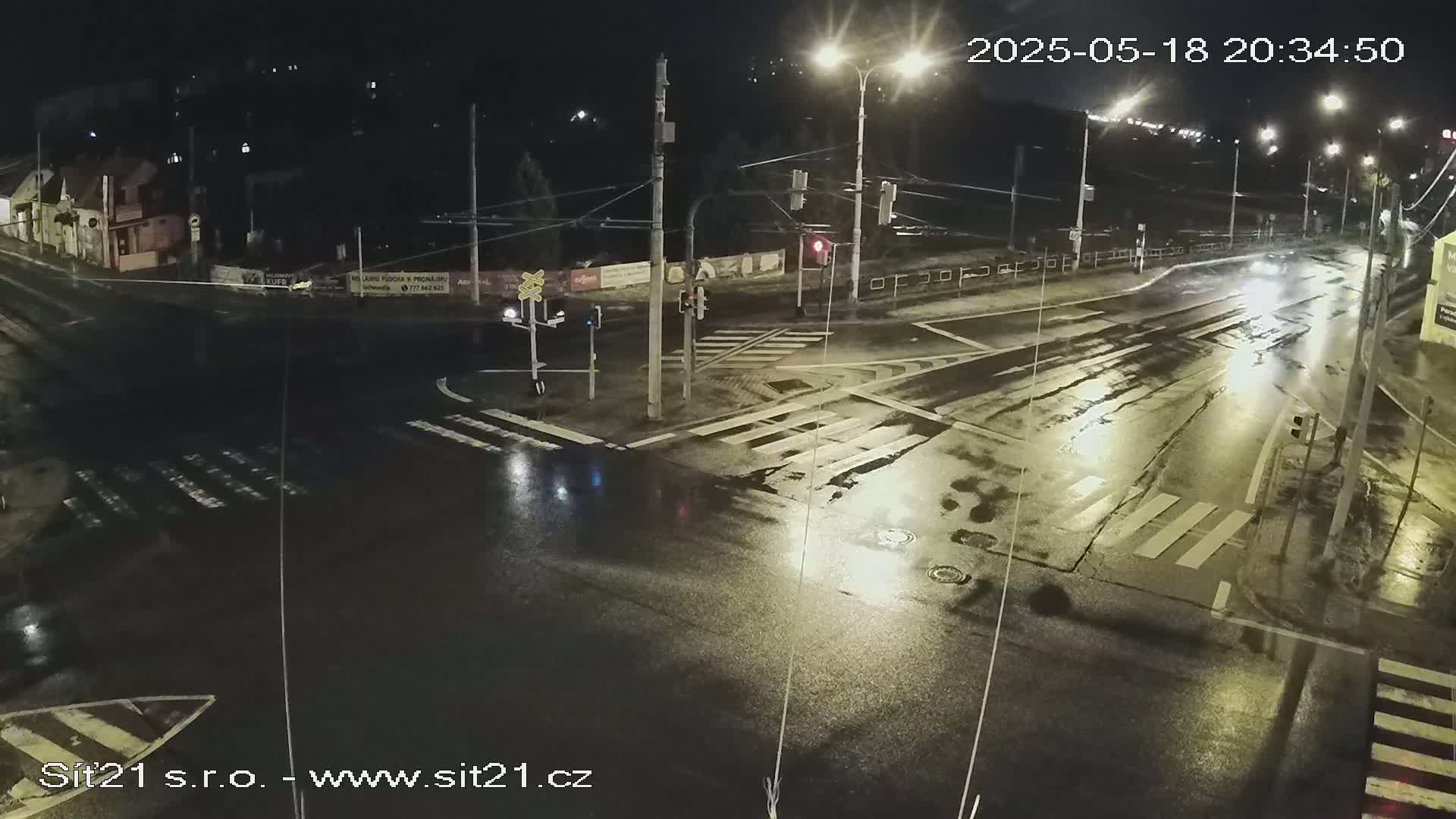 A wet, nighttime intersection with traffic signals and crosswalks, illuminated by streetlights.