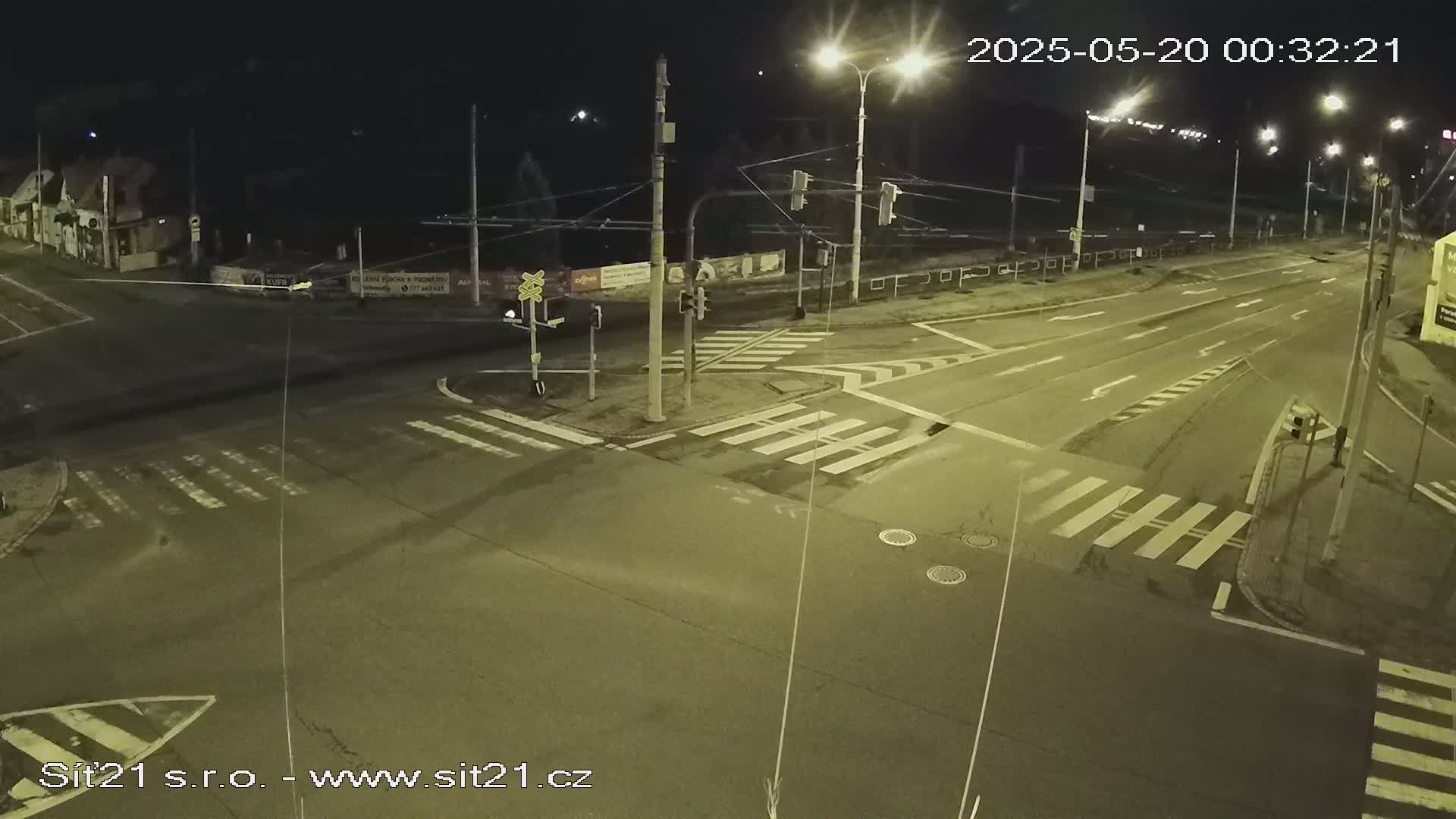 A nighttime view of a mostly empty road intersection with crosswalks and traffic signals under dark skies.