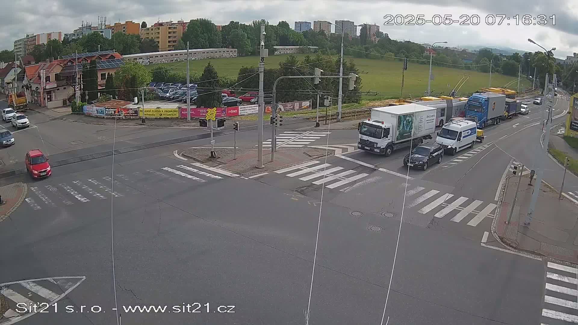 Several vehicles, including trucks and cars, are navigating a multi-lane intersection under overcast skies.