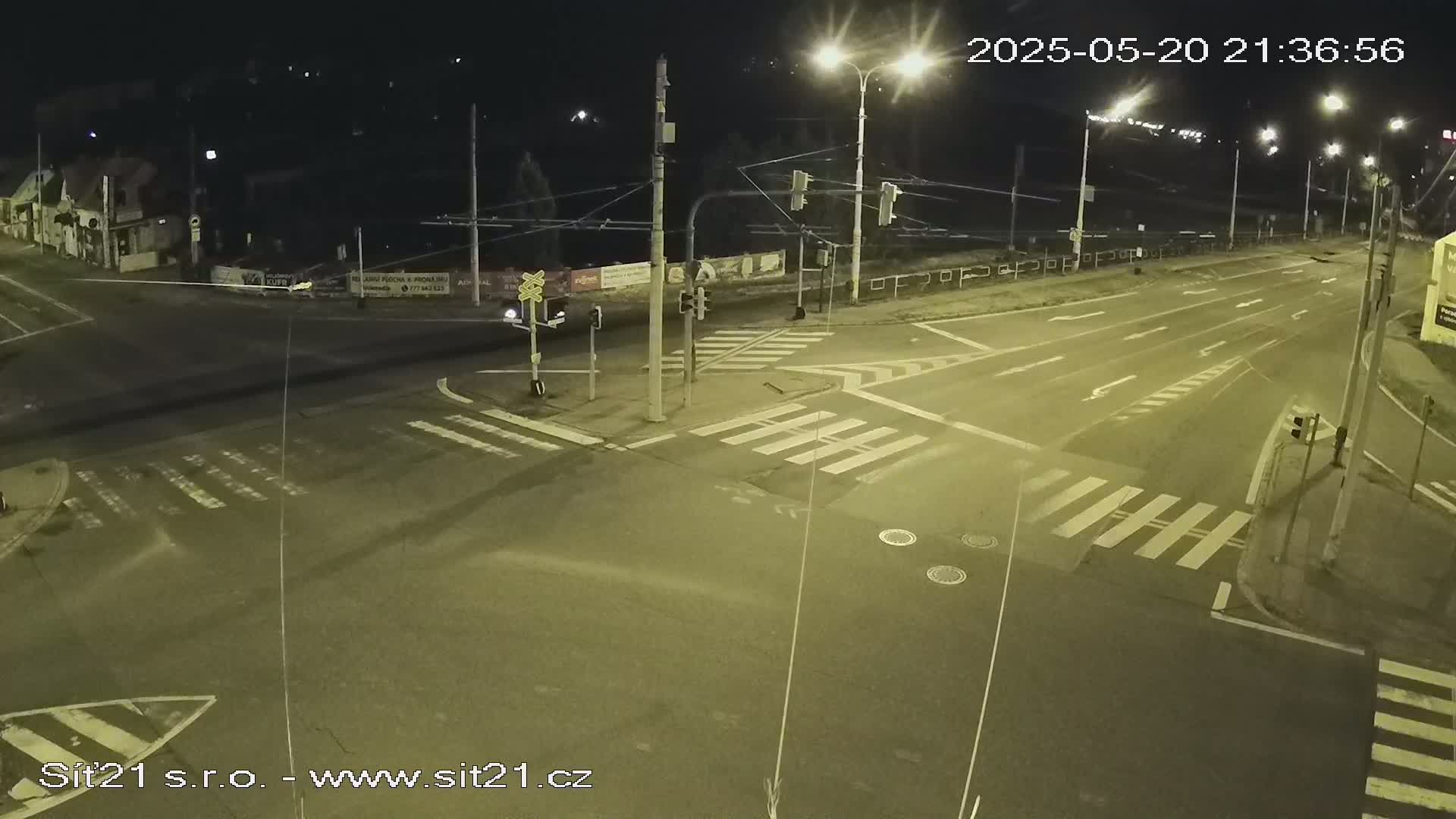 A nighttime view of a multi-lane road intersection with crosswalks and traffic signals, under clear skies.