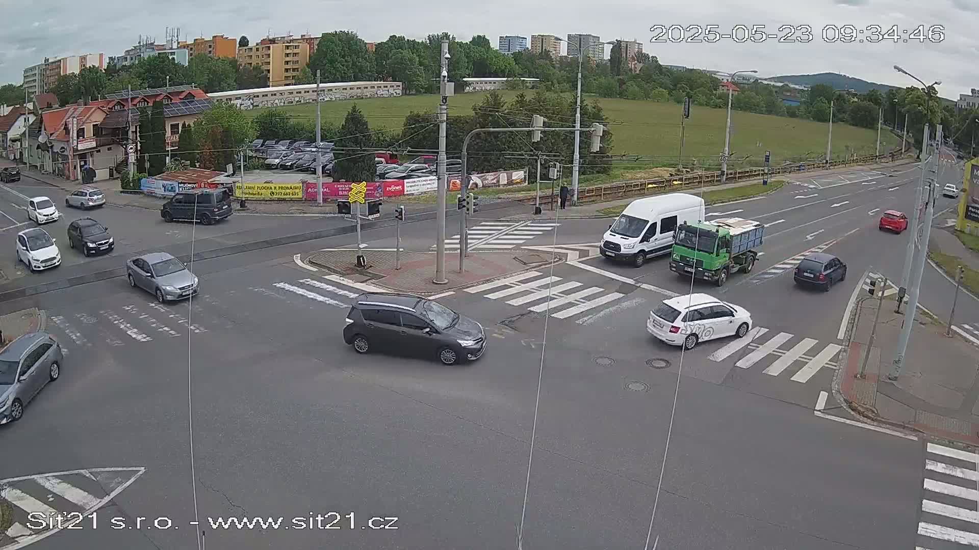 A street intersection with several cars and trucks navigating a crosswalk under an overcast sky.