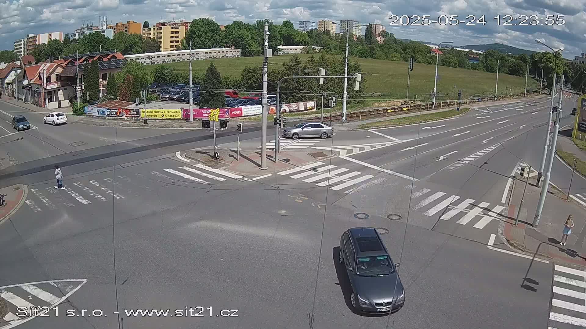 A partly cloudy day shows a street intersection with several cars and pedestrians, with one car turning right.