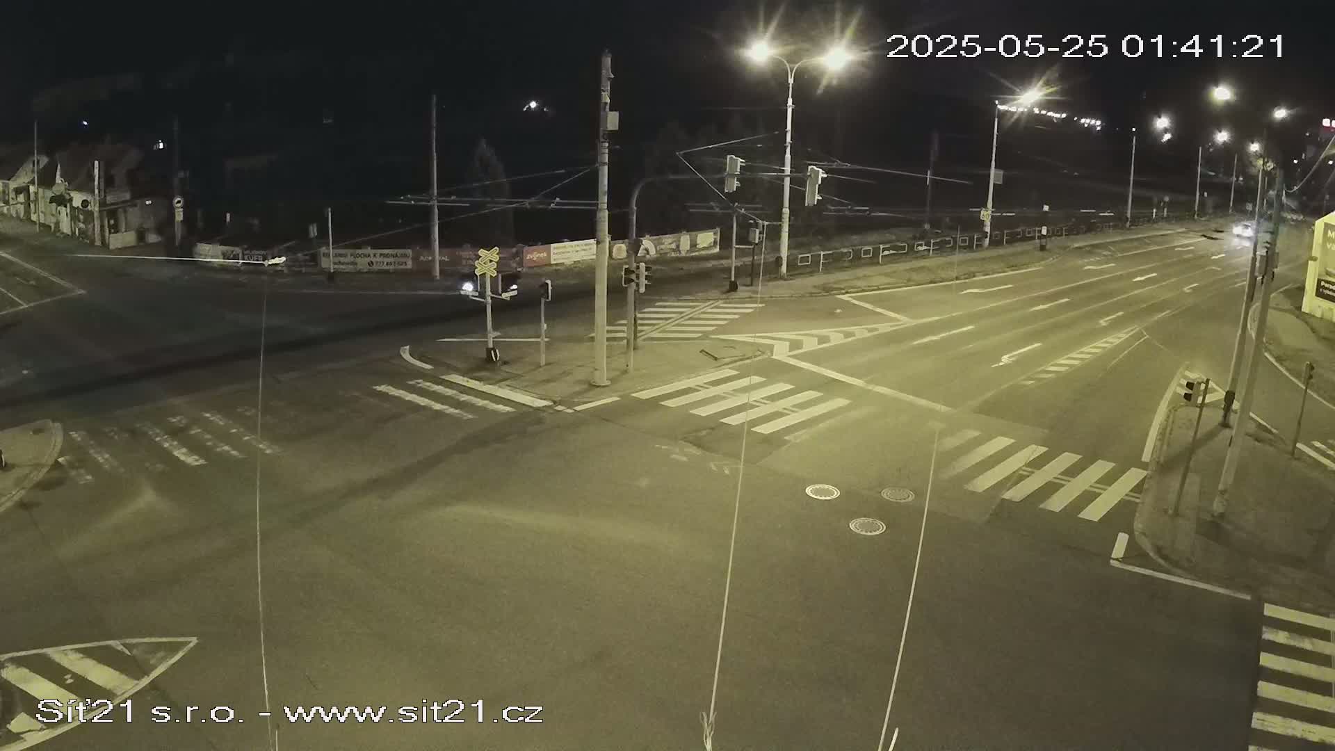 A nighttime view of a multi-lane road intersection with crosswalks, traffic lights, and a few vehicles.