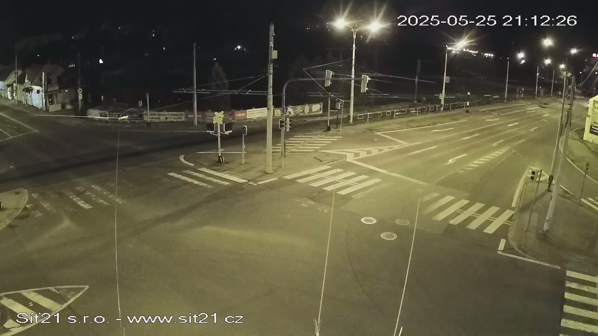 A nighttime view of a multi-lane road intersection with crosswalks and traffic lights, under clear skies.