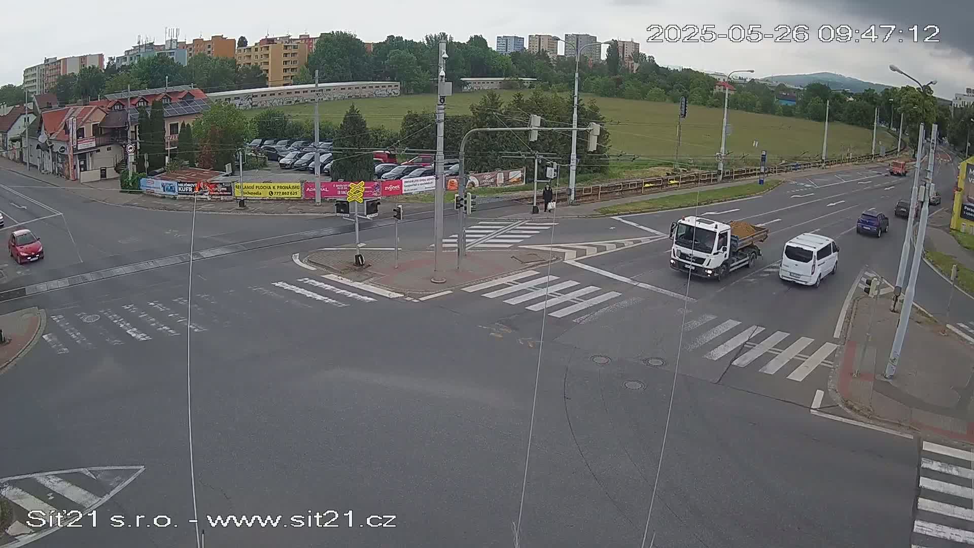 A high-angle view of a road intersection with several vehicles, including a truck and van, under an overcast sky.