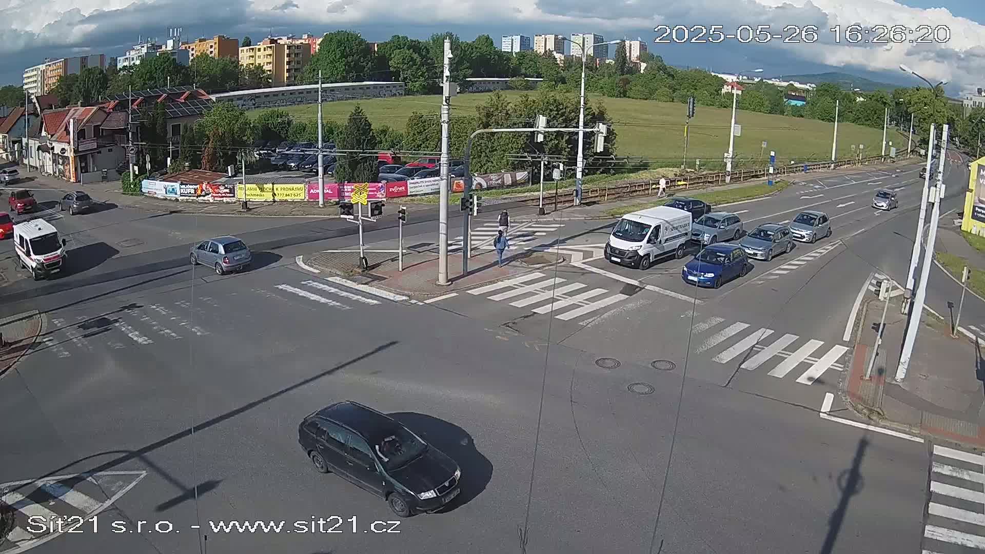 Several cars are driving through a multi-lane intersection on a partly cloudy day.