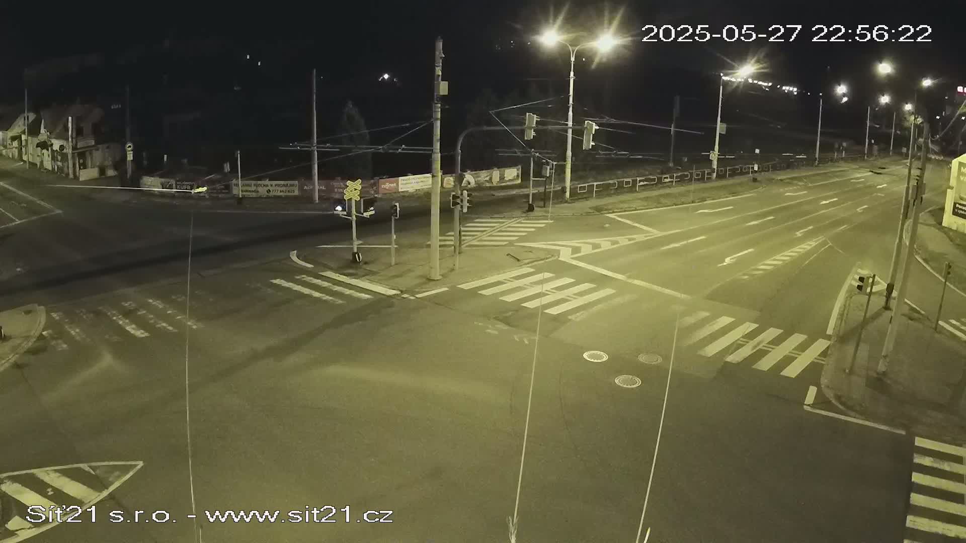 A nighttime view of a mostly empty street intersection with crosswalks, traffic lights, and overhead power lines.