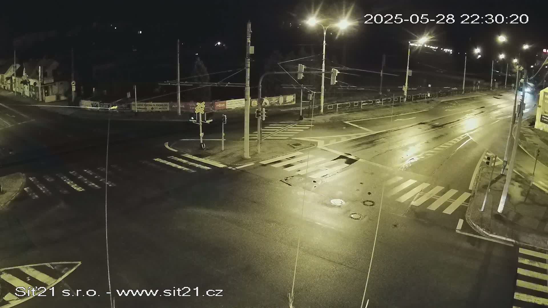 A wet, empty intersection at night is illuminated by streetlights.