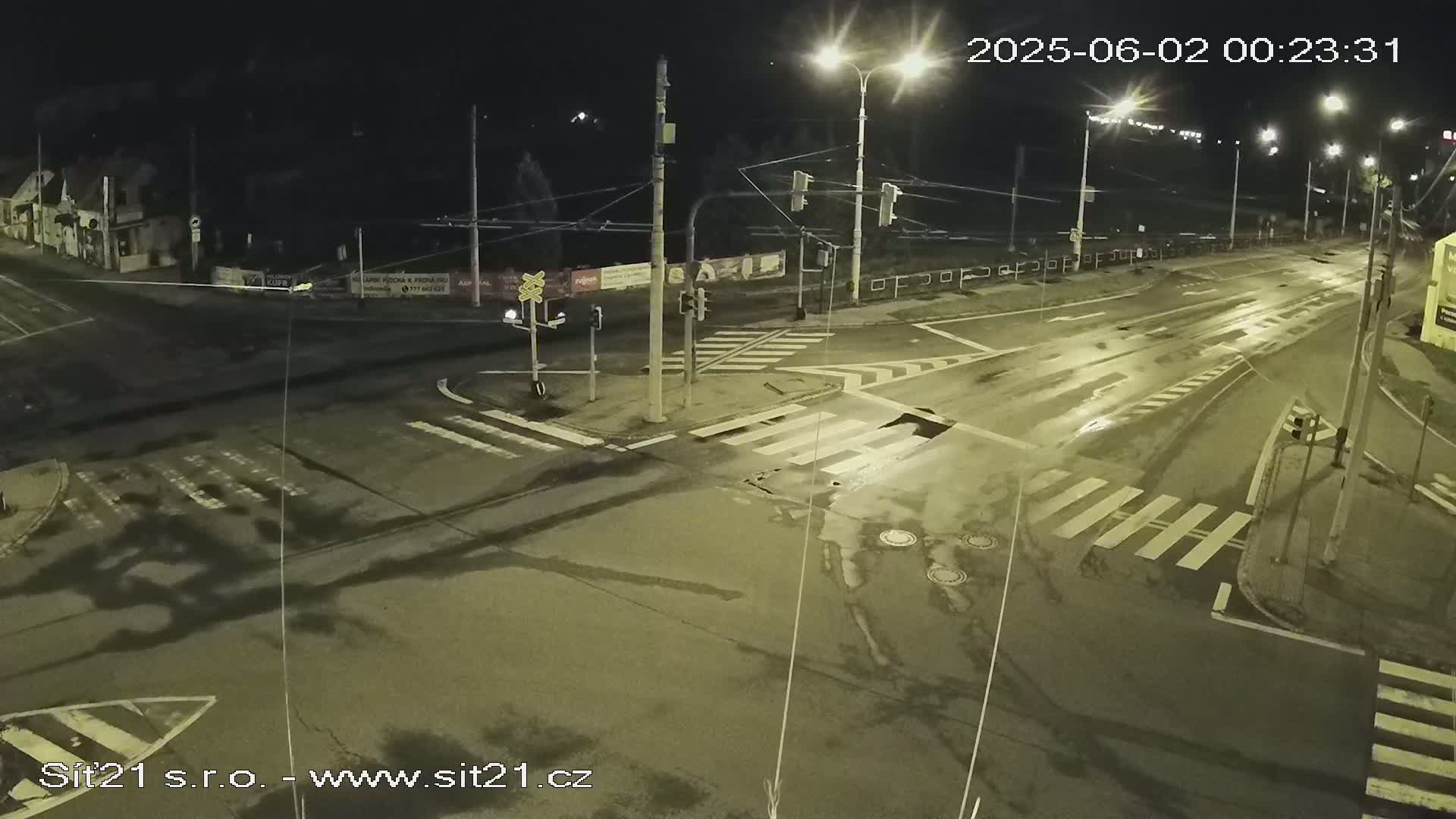 A wet, empty street intersection at night, illuminated by streetlights, shows crosswalks and traffic signals.