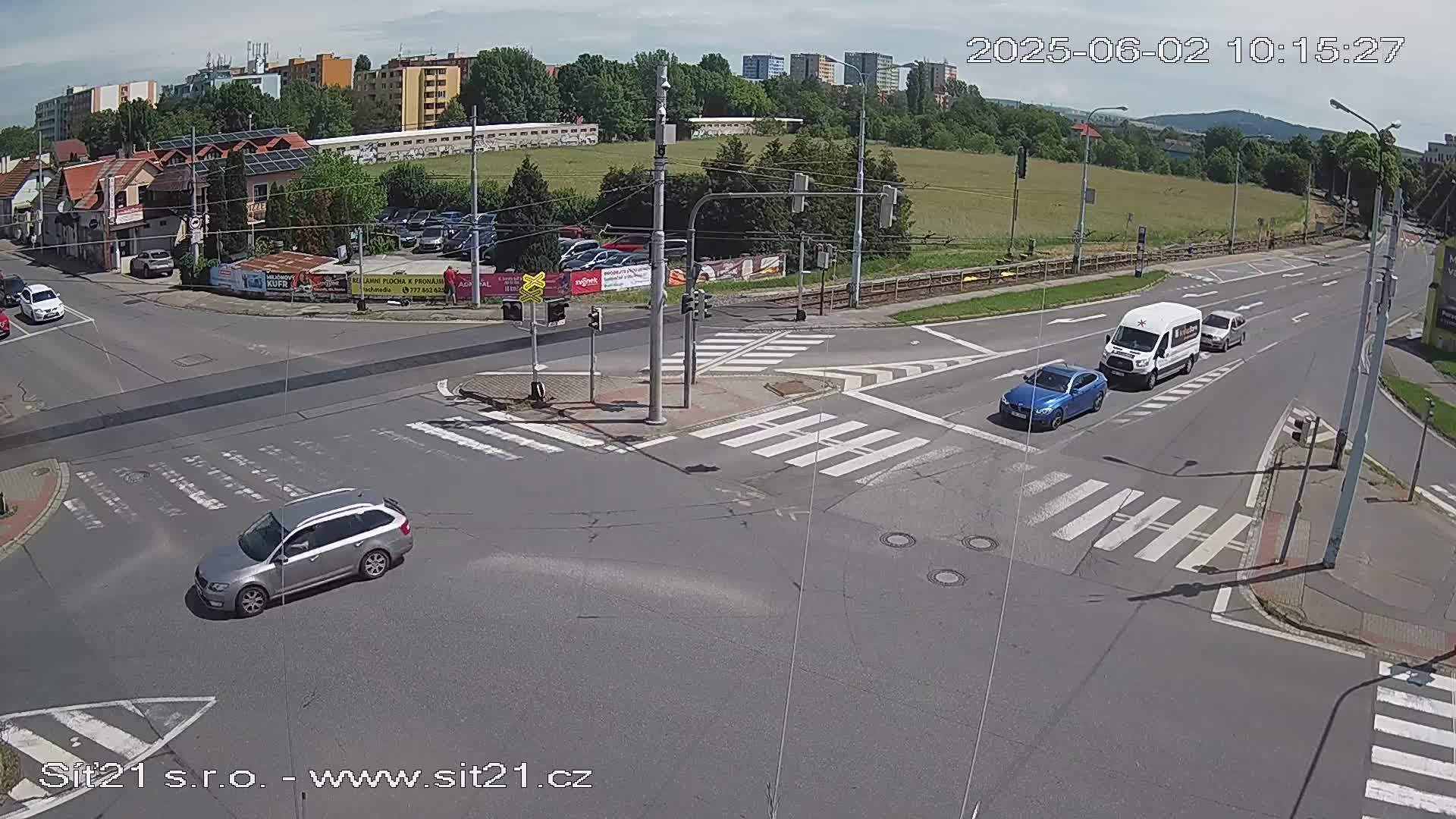 A high-angle view of a multi-lane road intersection on a sunny day with several cars and a van at the crossing.