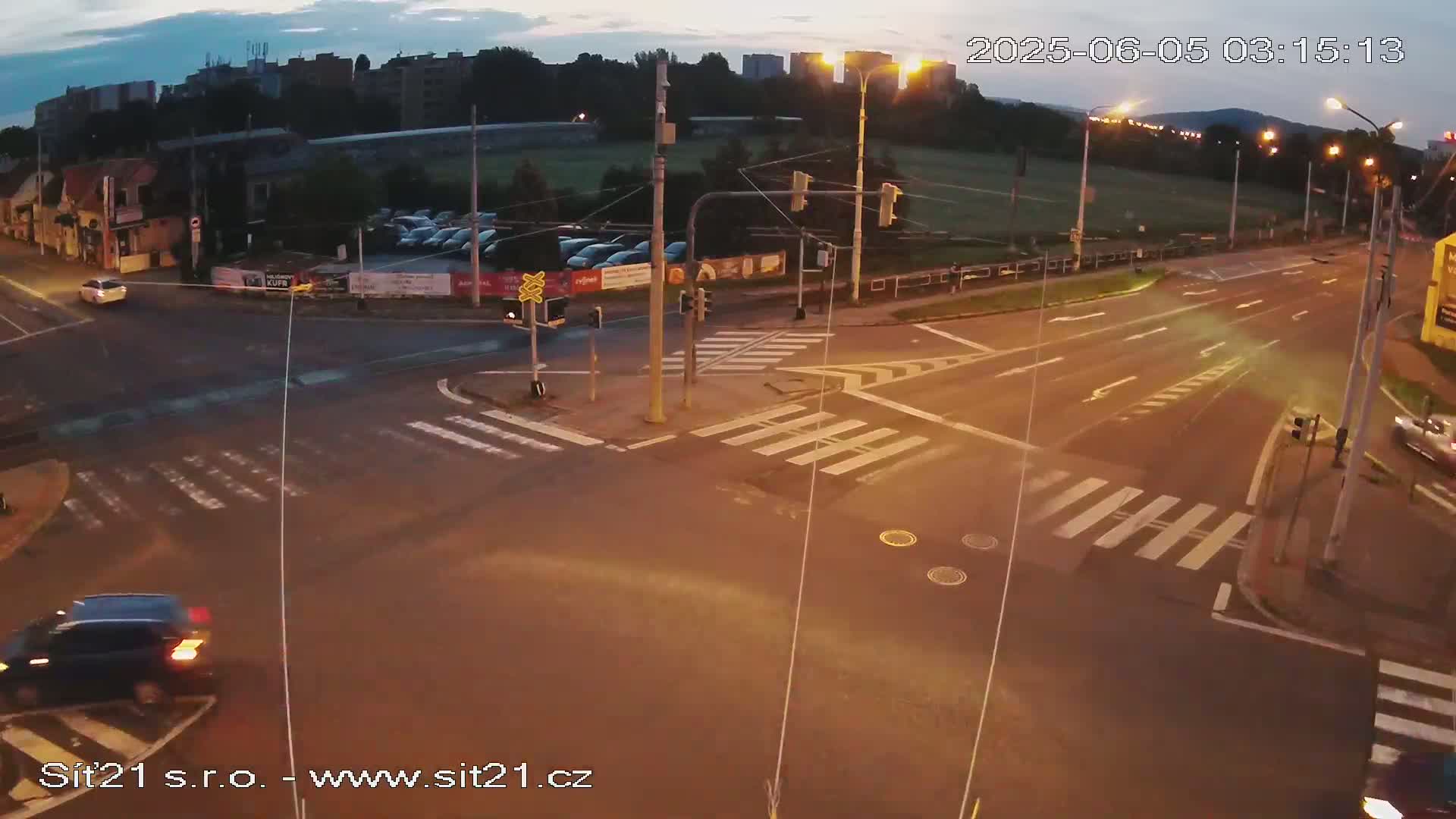 A nighttime, high-angle view of a multi-lane road intersection with crosswalks, traffic signals, and a few cars.