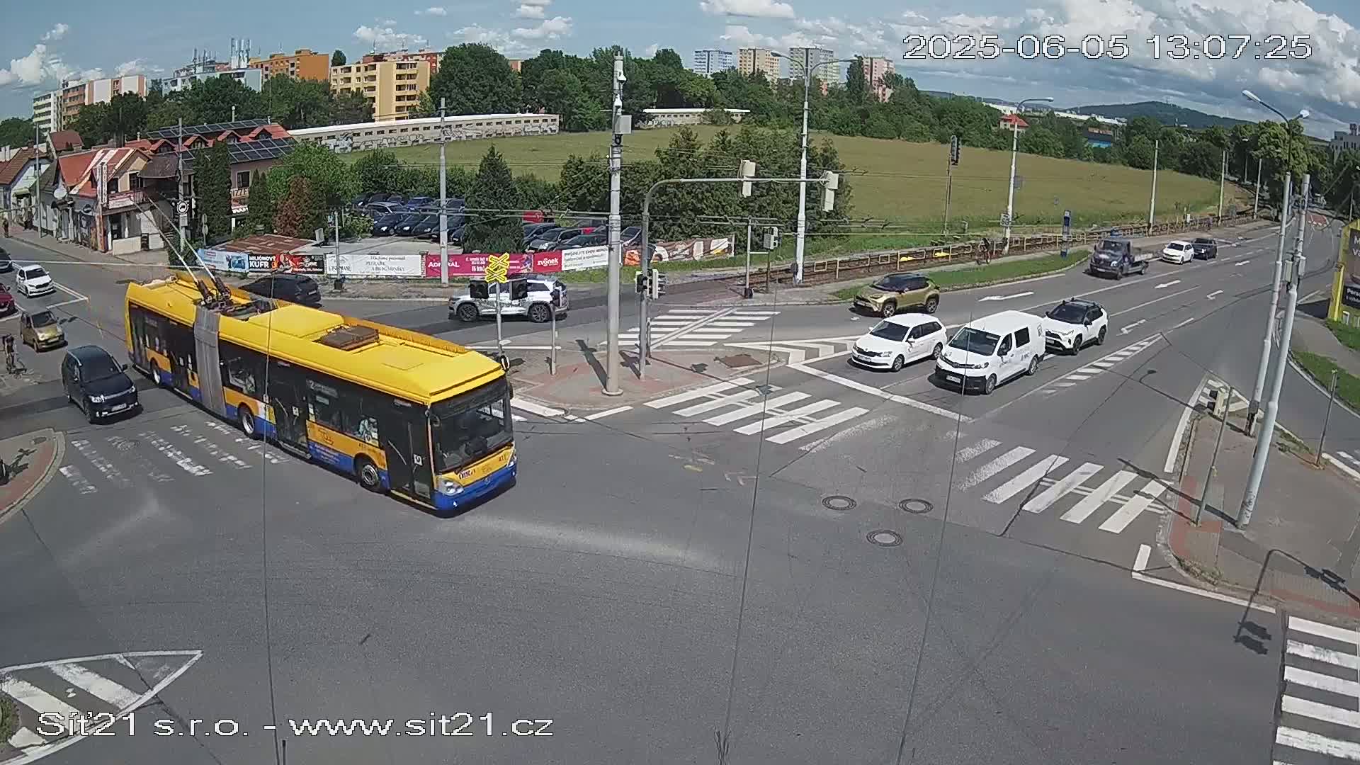 A yellow trolleybus and several cars are at a multi-lane intersection on a sunny day.