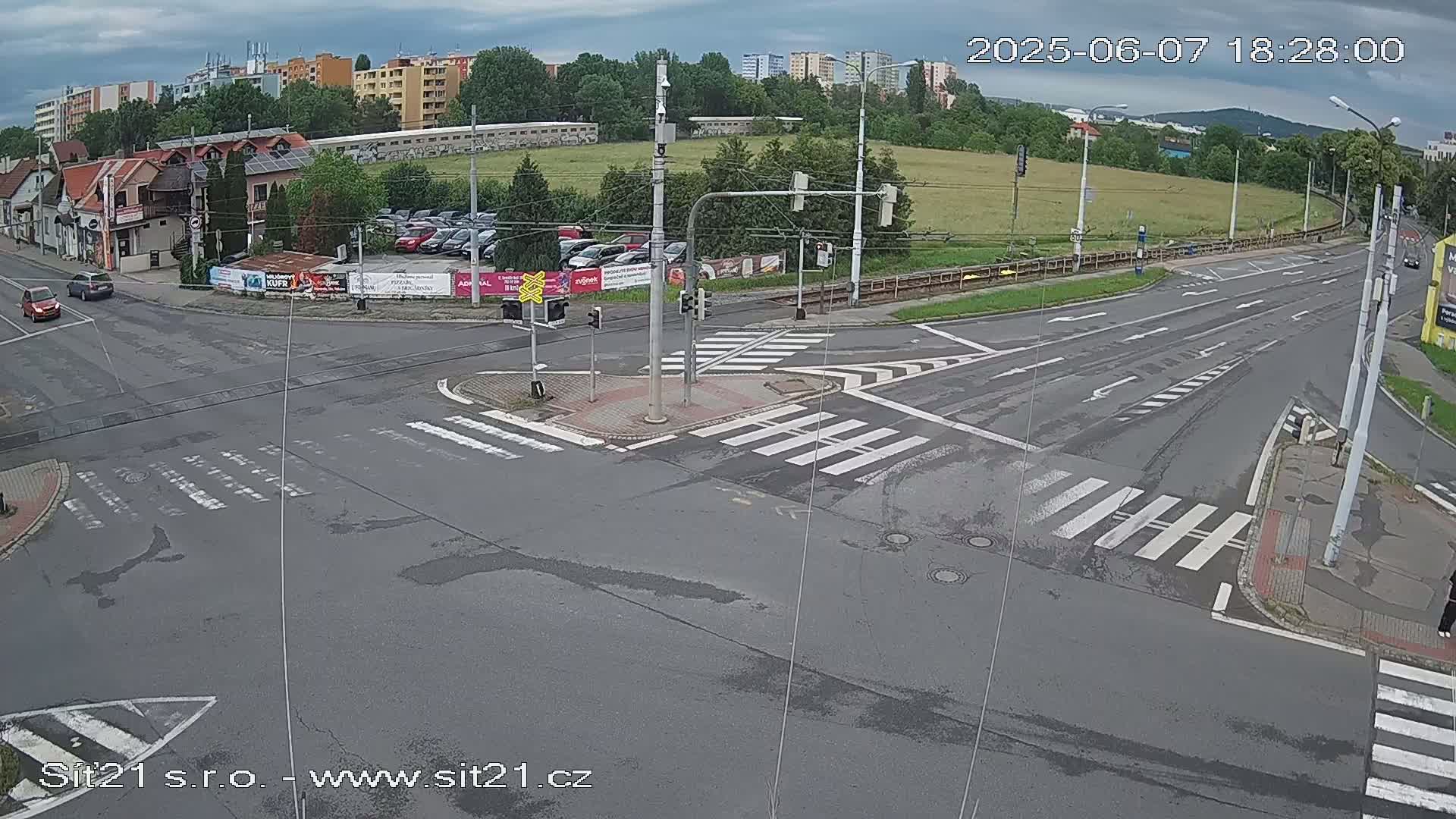 A mostly empty road intersection with crosswalks and traffic signals under a cloudy sky.