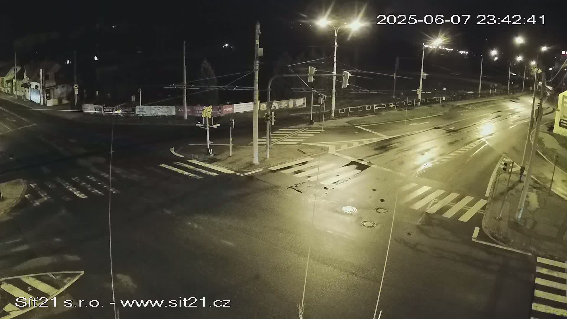A wet, empty intersection at night is illuminated by streetlights.