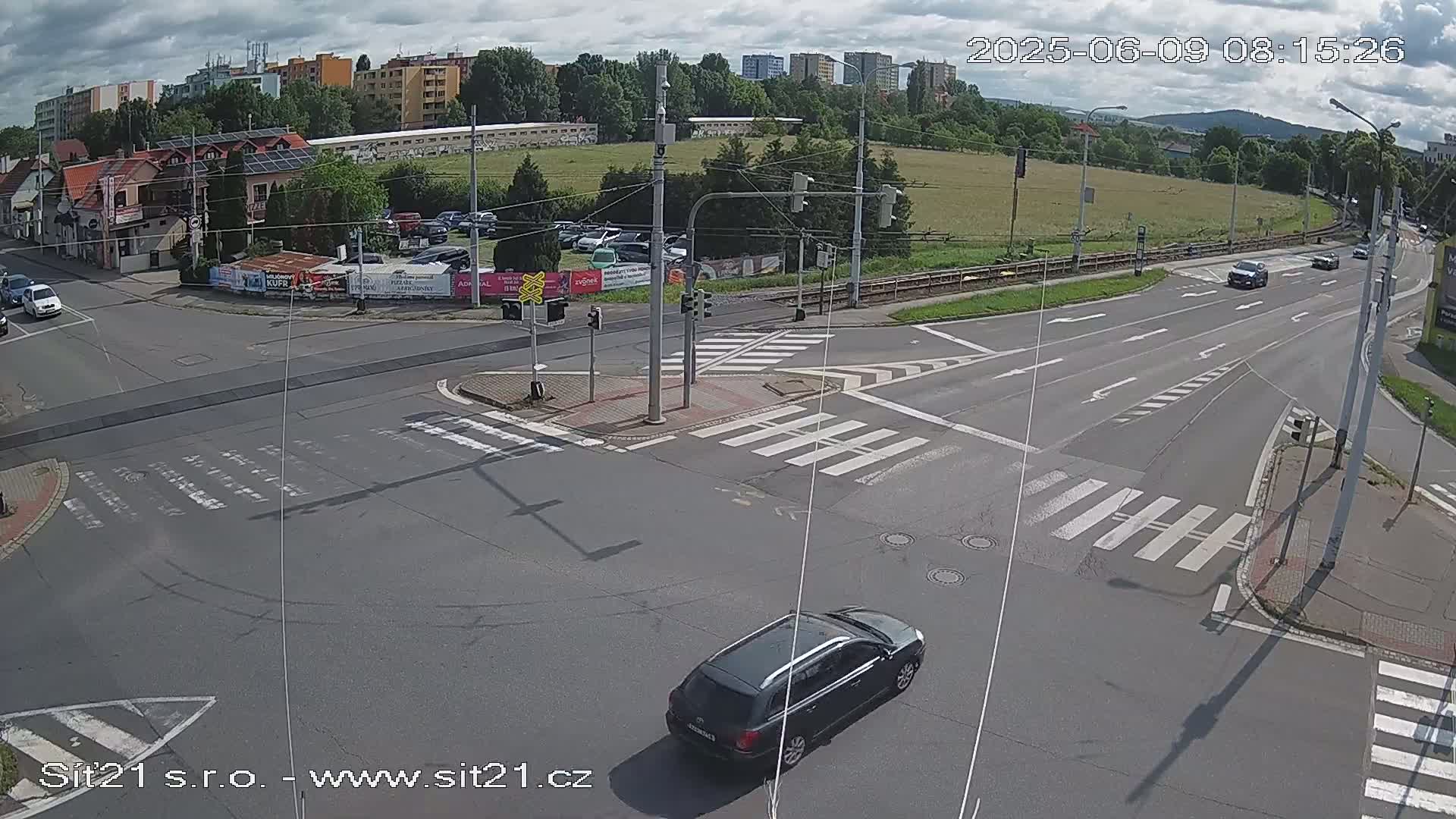A high-angle view of a multi-lane road intersection with several cars, under partly cloudy skies.