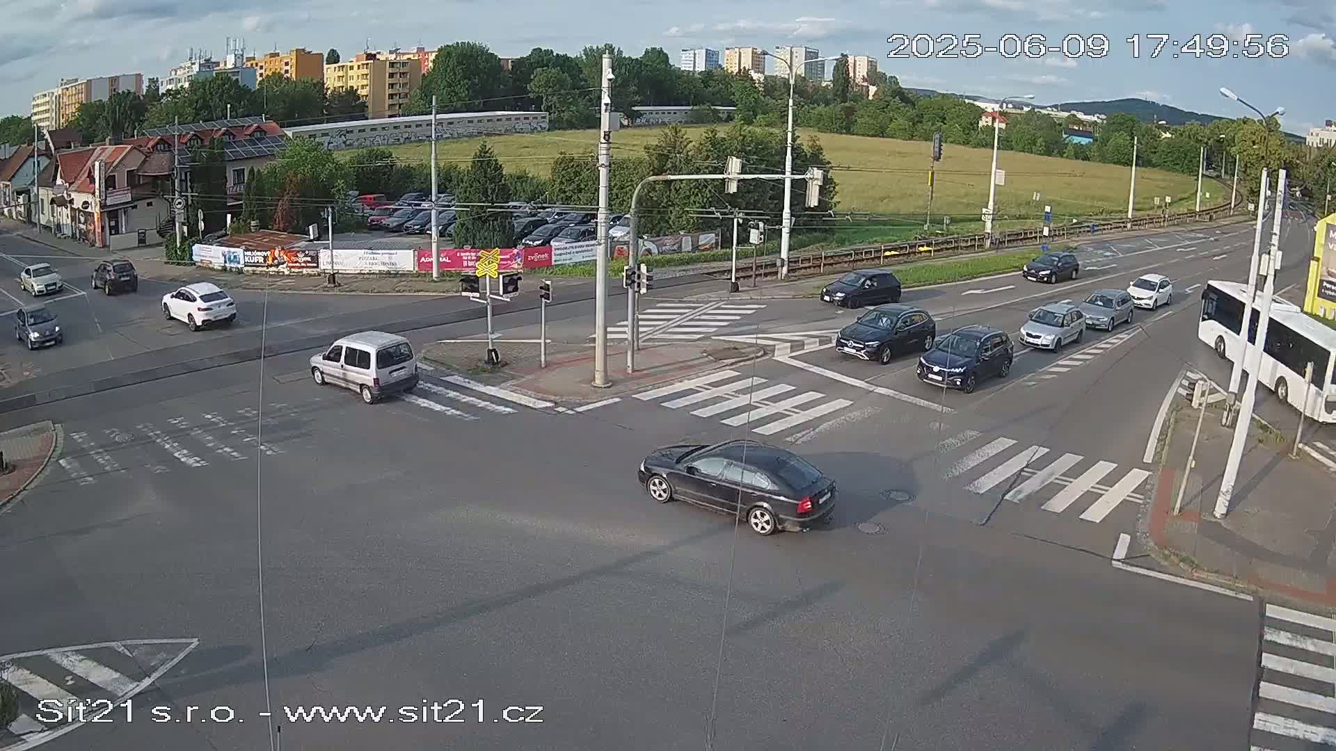 Several cars and a bus navigate a multi-lane intersection under partly cloudy daytime skies.