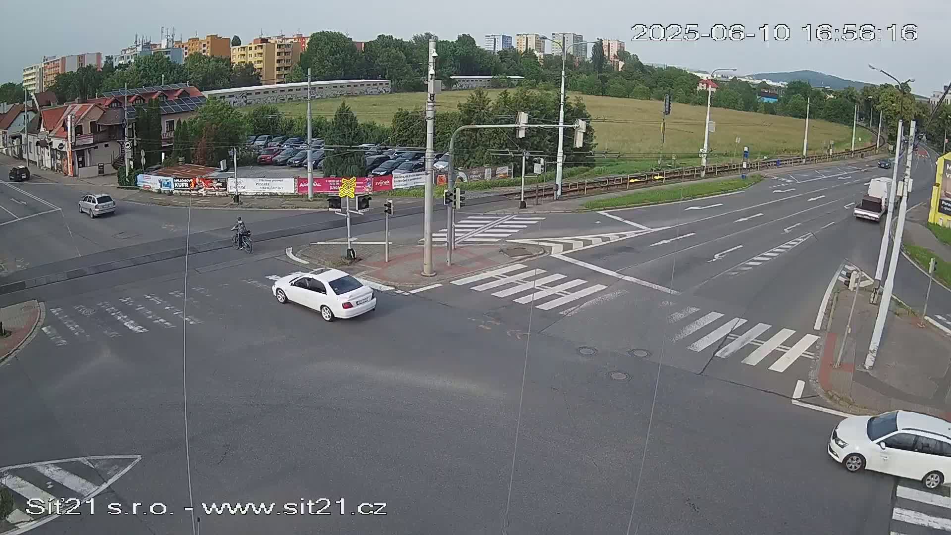 A high-angle, long shot of a street intersection with several vehicles and a cyclist, under overcast skies.