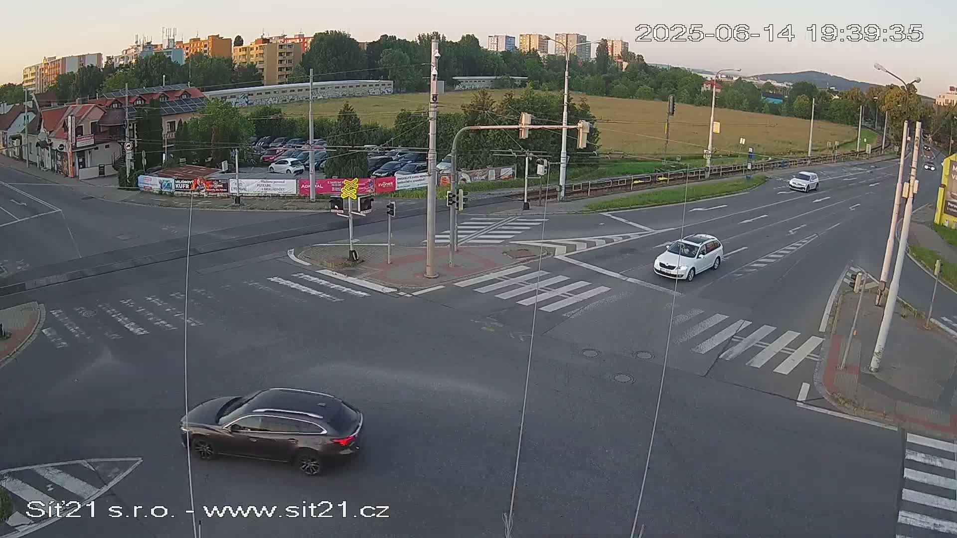 A sunny day at a multi-lane intersection shows several cars, a cyclist, and buildings in the background.