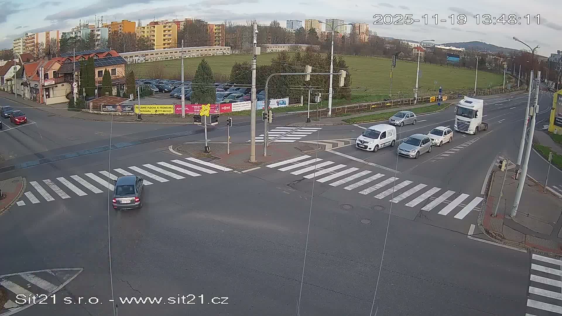 A dark-colored car drives through a well-lit intersection at night.