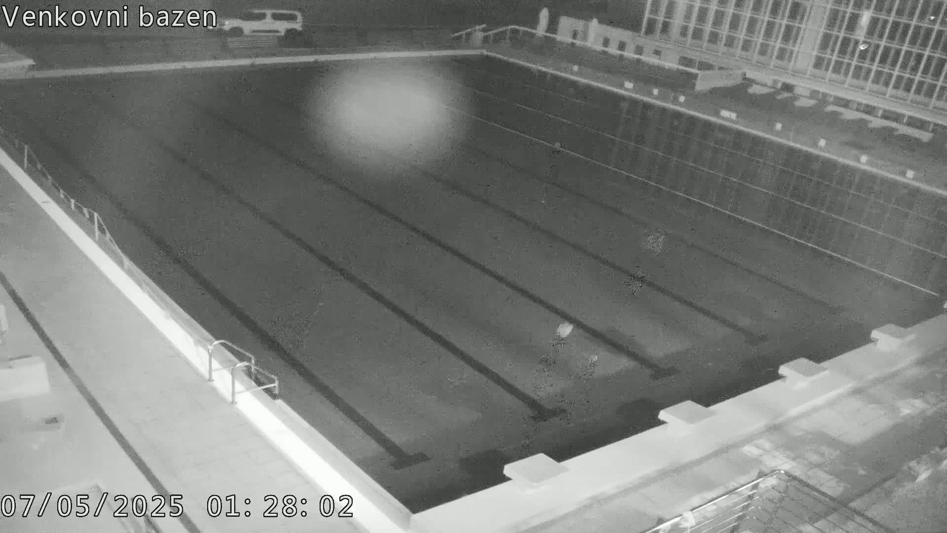 An empty, dark outdoor swimming pool is seen at night.