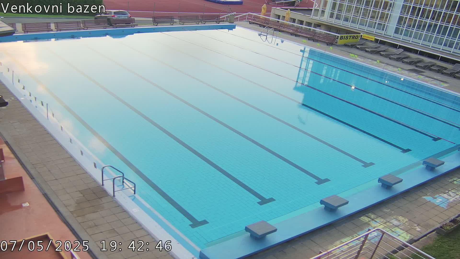 An outdoor, empty swimming pool with multiple lanes is shown under a clear sky.