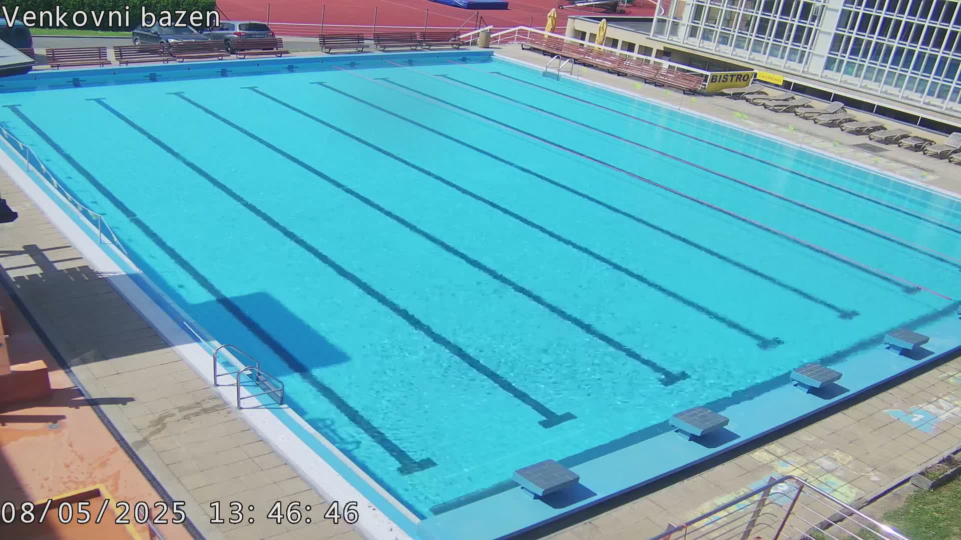 A sunny outdoor view of an empty, light blue swimming pool with multiple lanes and starting blocks.