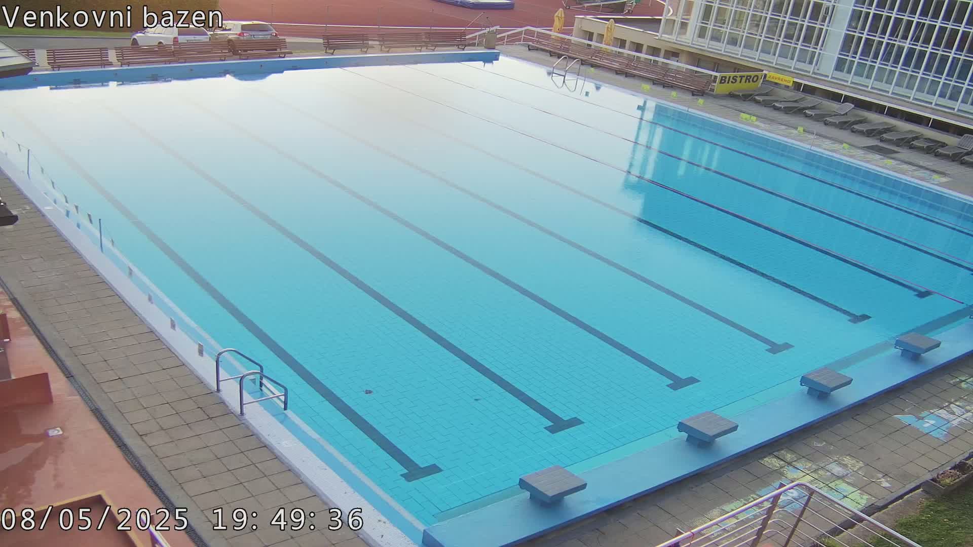 An outdoor, empty swimming pool with multiple lanes is shown on a mostly clear day.