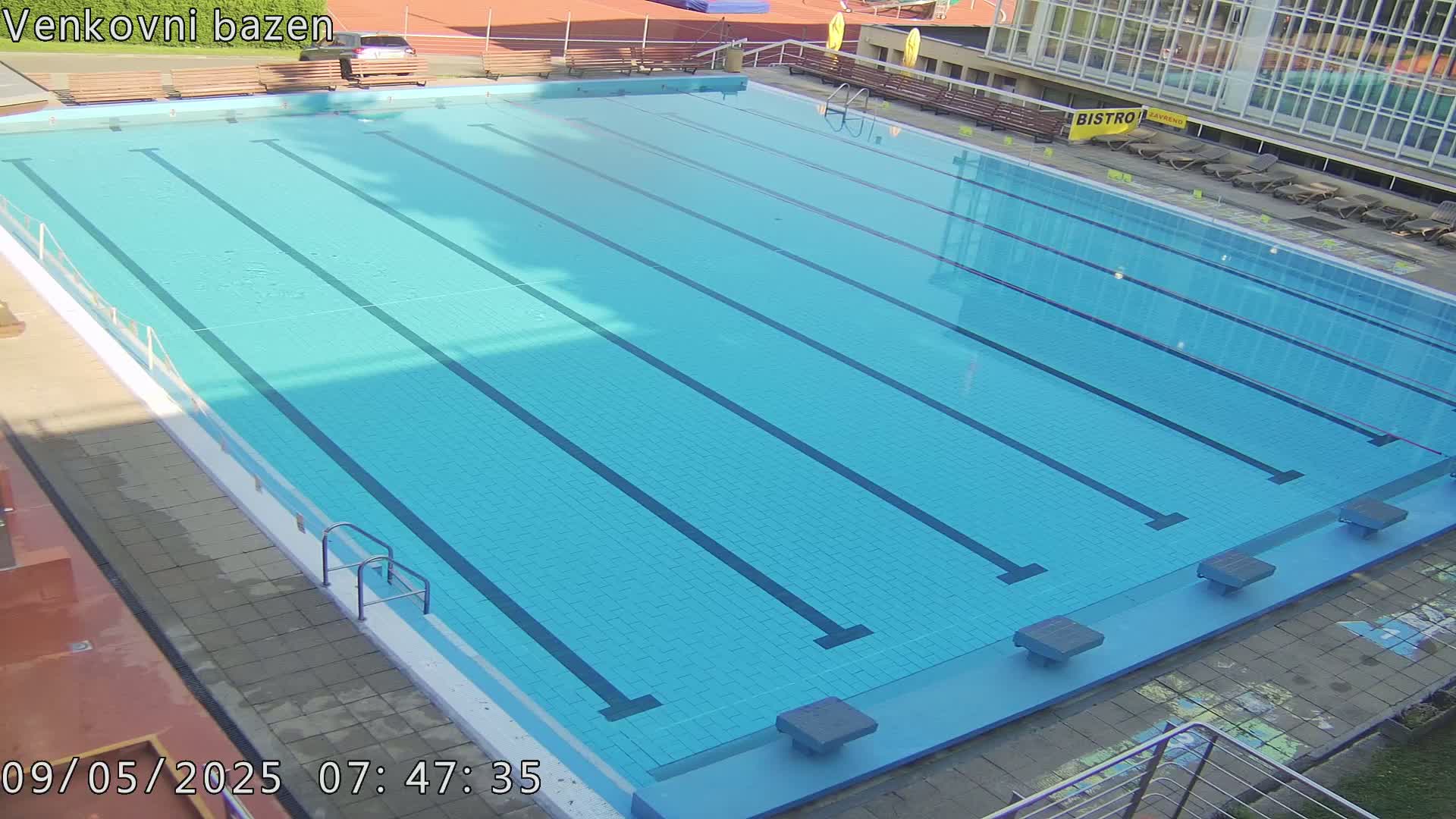 An outdoor swimming pool with multiple lanes is mostly empty on a sunny day.