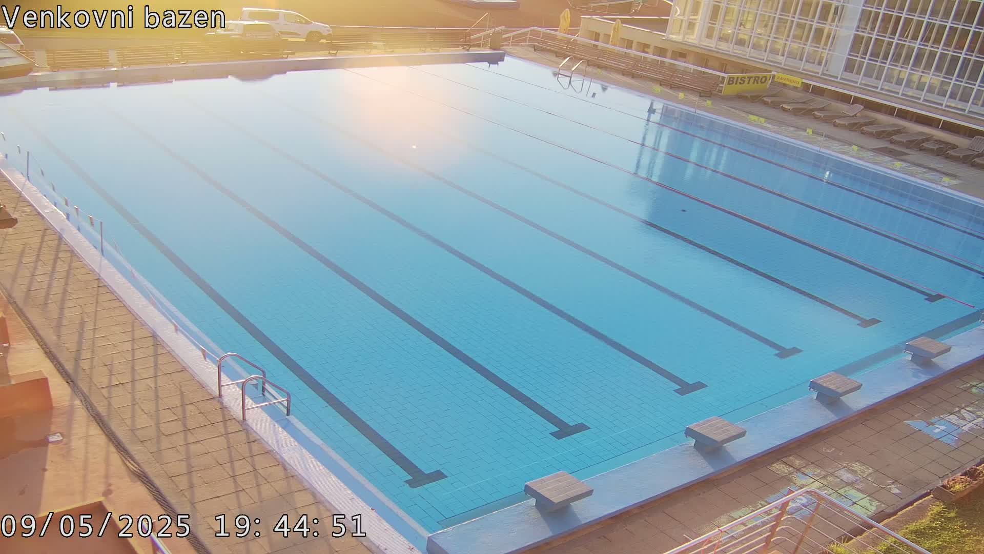 An outdoor swimming pool with multiple lanes is bathed in sunlight.