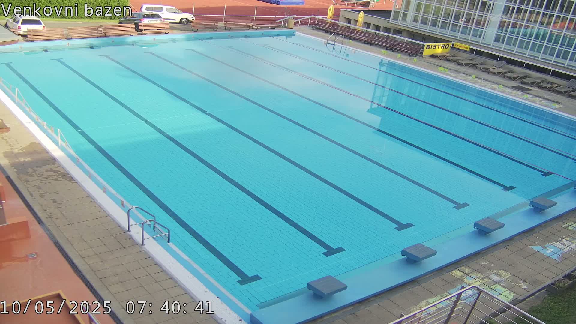 An outdoor swimming pool with several lanes is mostly empty on a sunny day.
