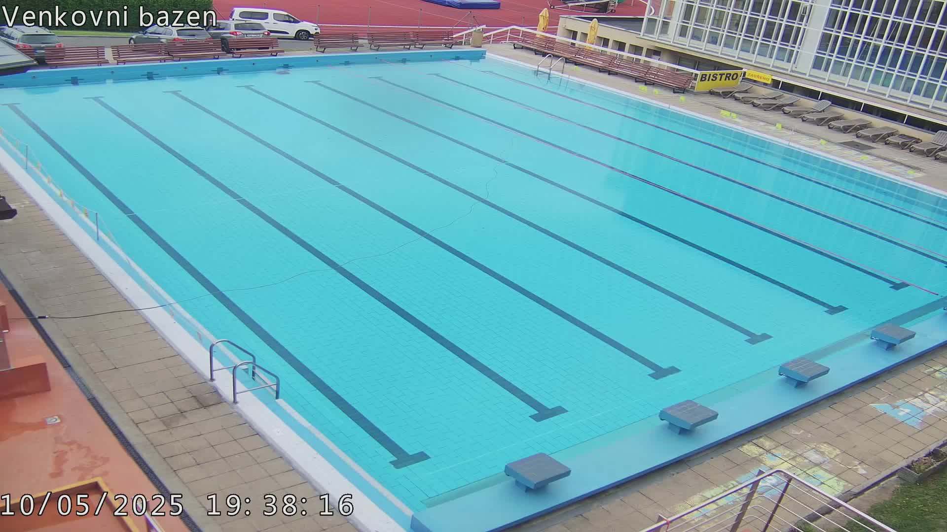 An outdoor swimming pool with multiple lanes is empty under a mostly clear sky.