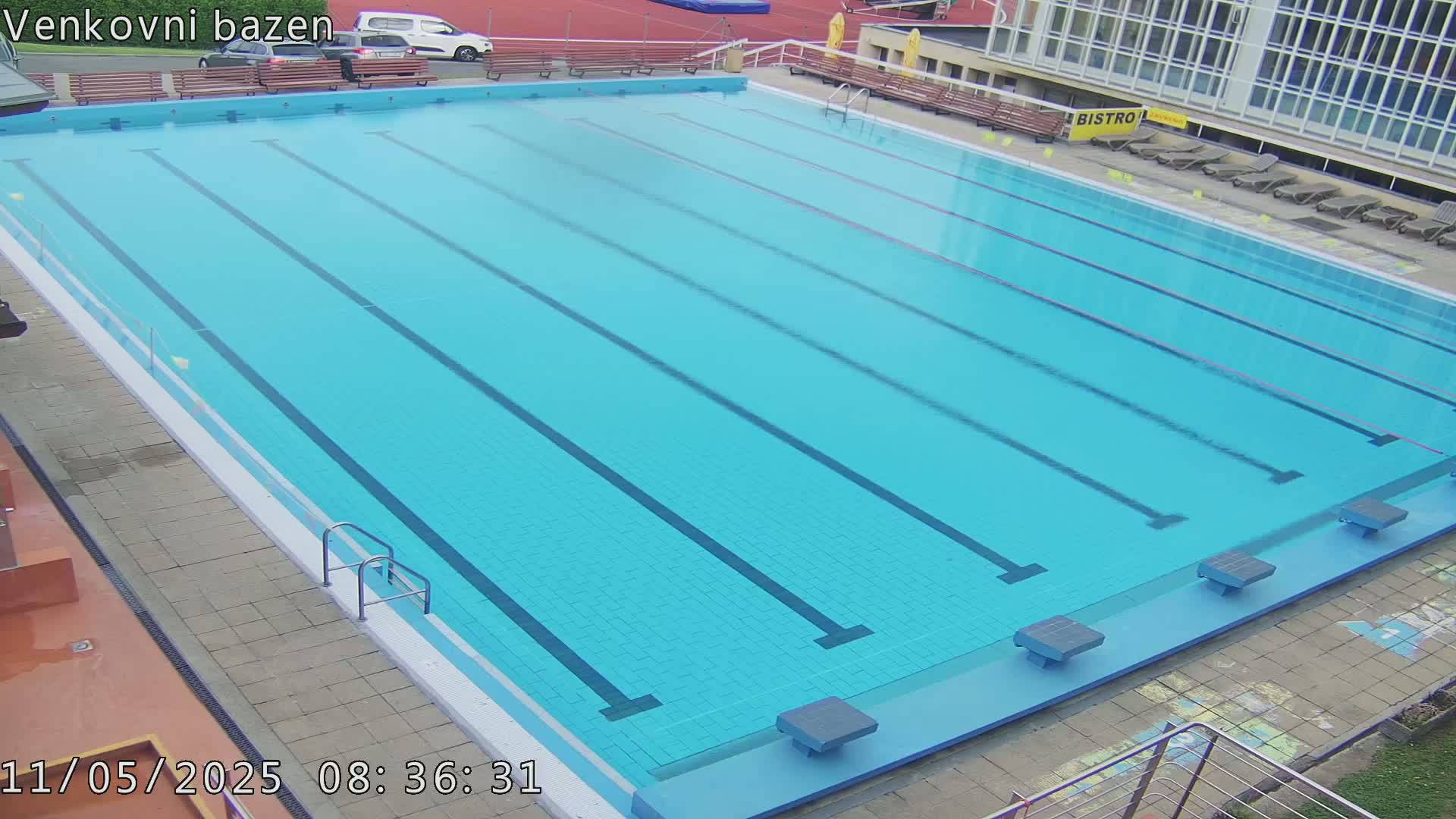 An outdoor swimming pool with multiple lanes is empty on a seemingly clear day.